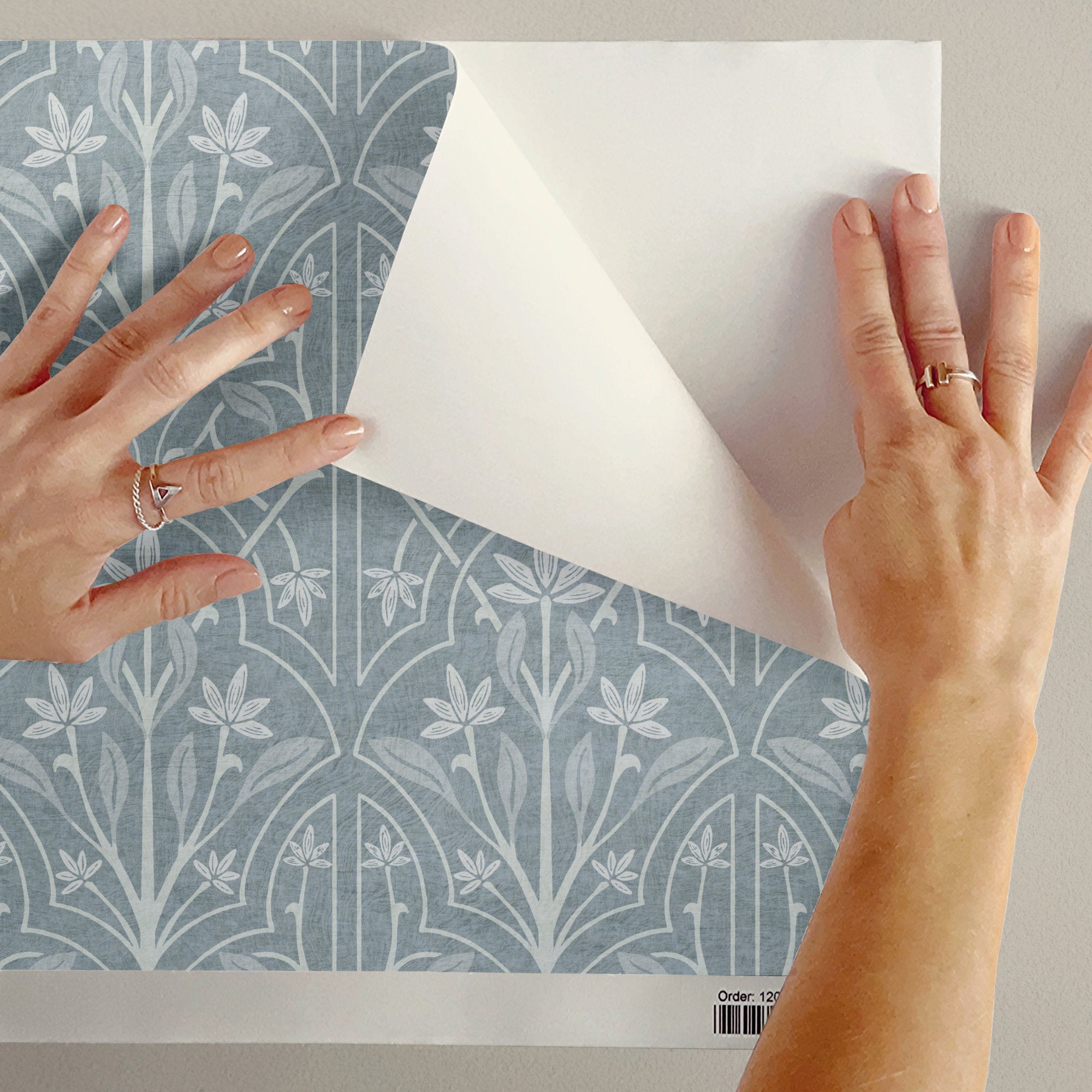 Blue and White Art Nouveau Trellis Wallpaper showing hands peeling away the top layer of patterned wallpaper.