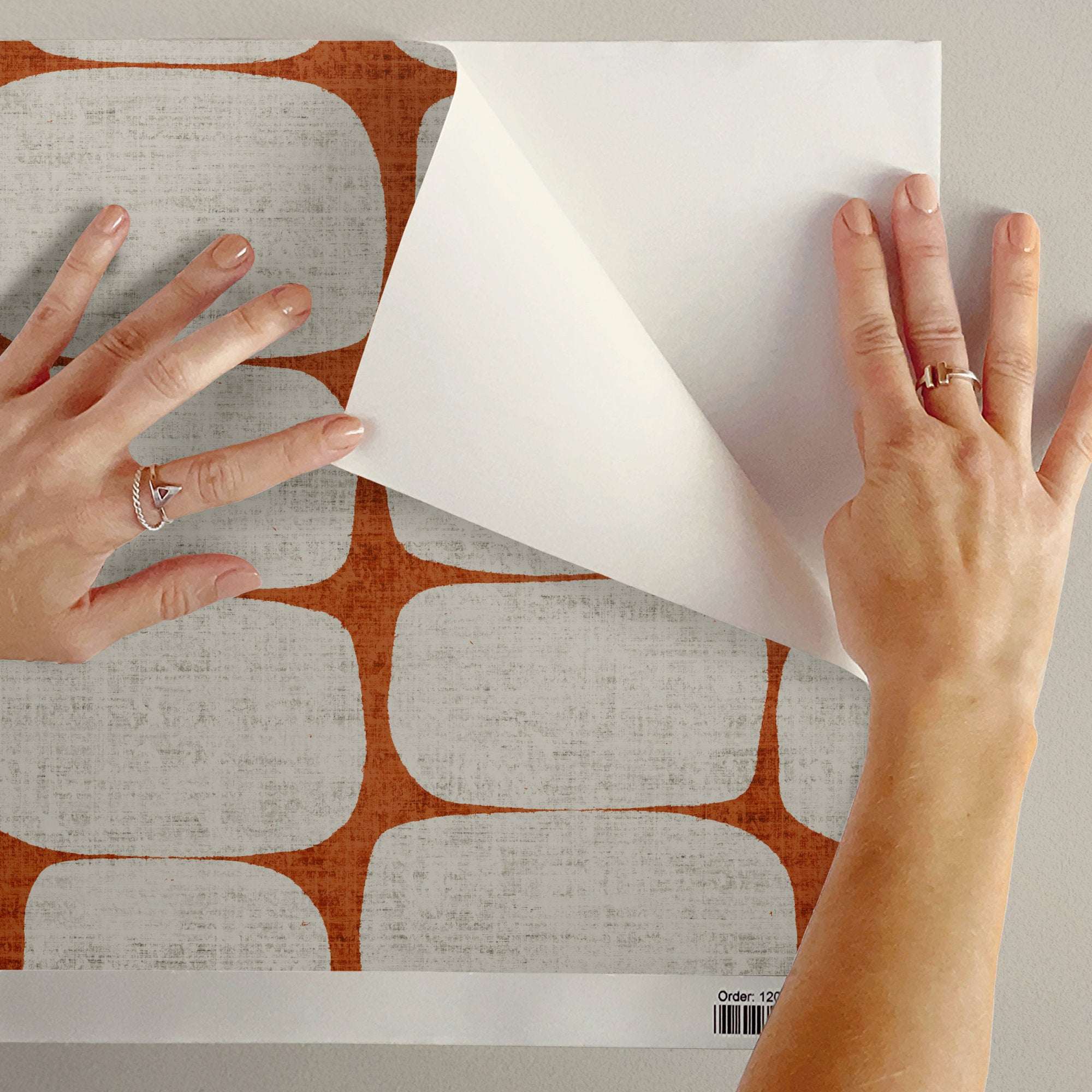 Wallpaper sheet held up, featuring orange geometric pebble stripe pattern of rounded rectangles.