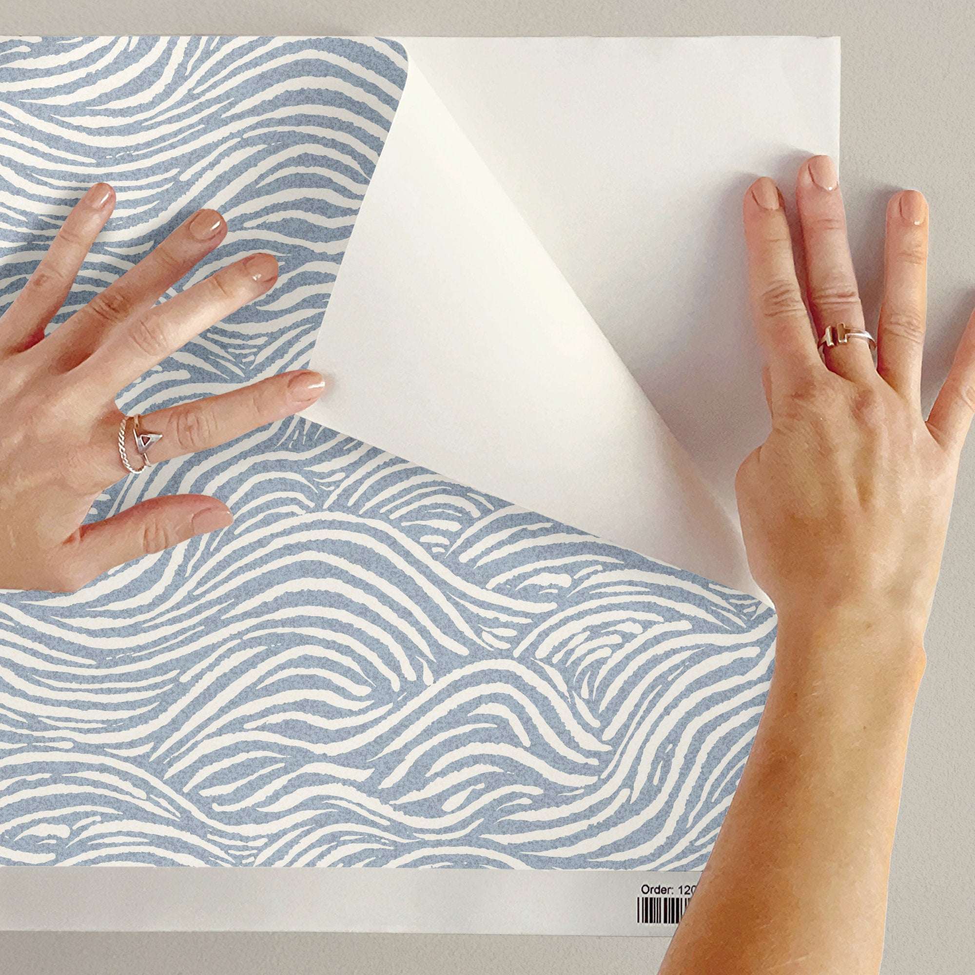 Wave-pattern wallpaper sheet with light blue wavy lines, hands aligning it