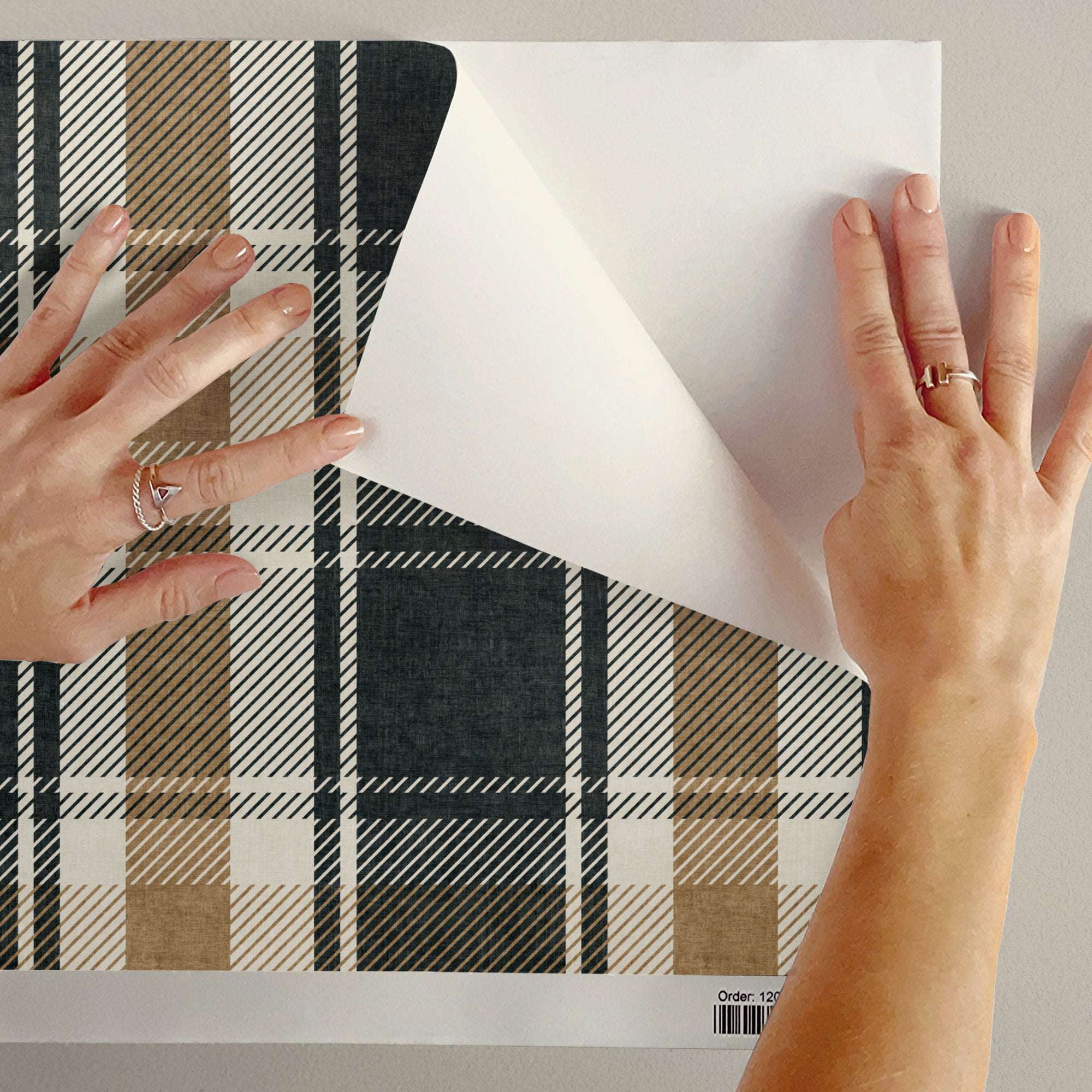 Hands applying tartan plaid wallpaper sheet showing cream and dark navy grid pattern