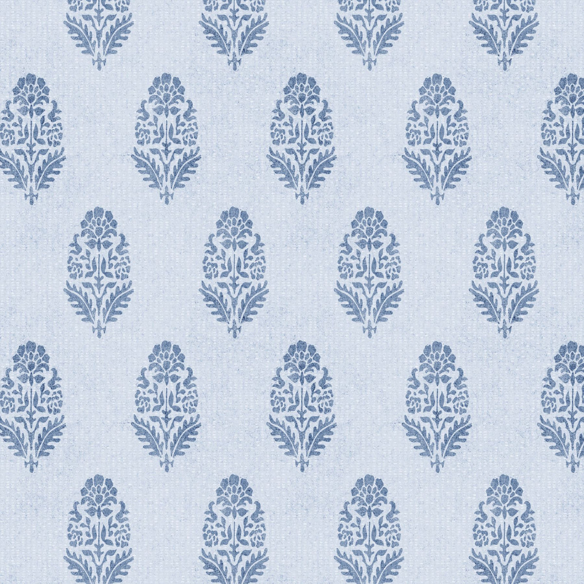 A close-up of denim blue floral block print wallpaper on a pale blue-white background. Small stylised bouquets of petals and leaves repeat in softly offset rows, with a slightly inky, textured edge.