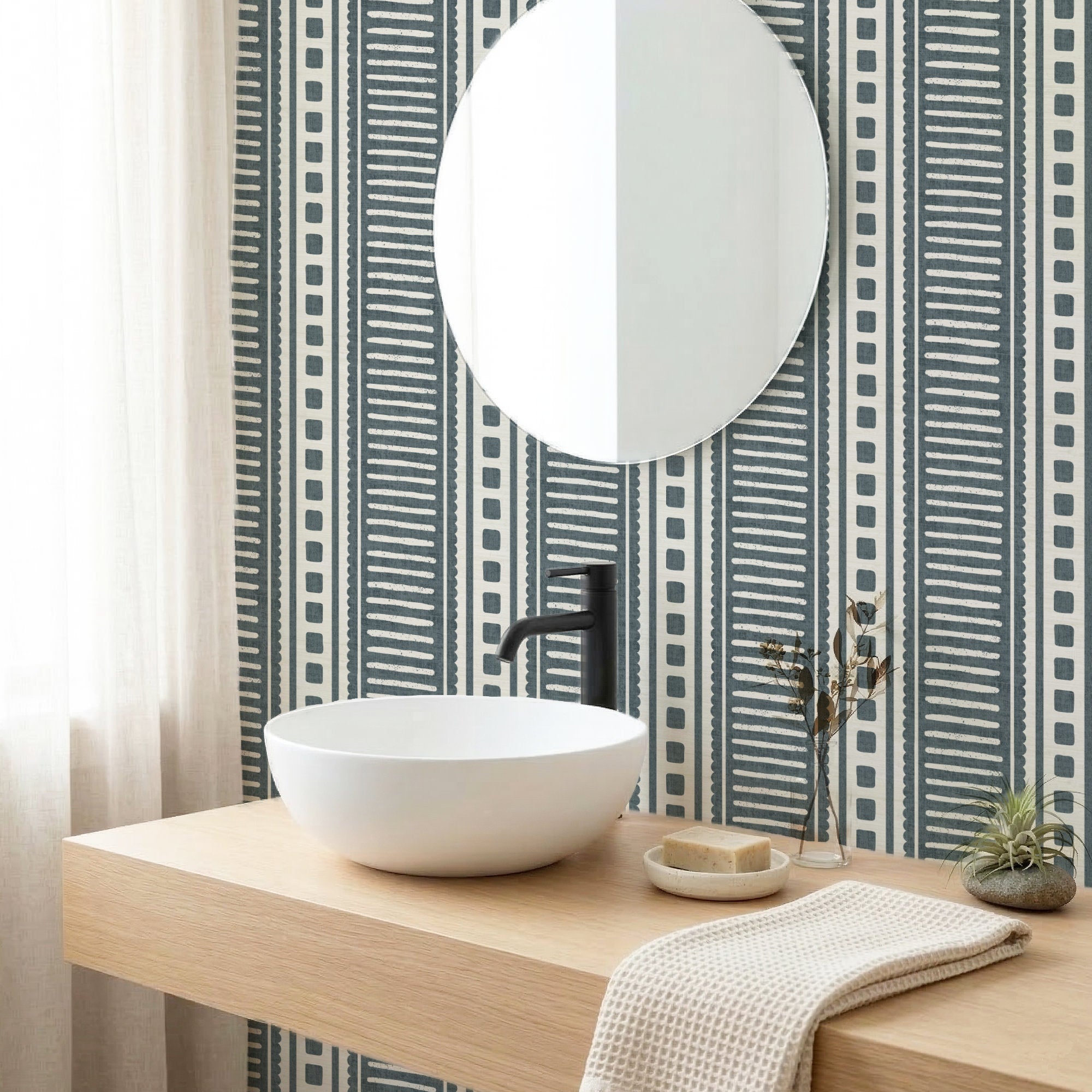 Dark slate blue coastal stripe wallpaper in a bathroom behind a round mirror and white vessel basin on a wood vanity