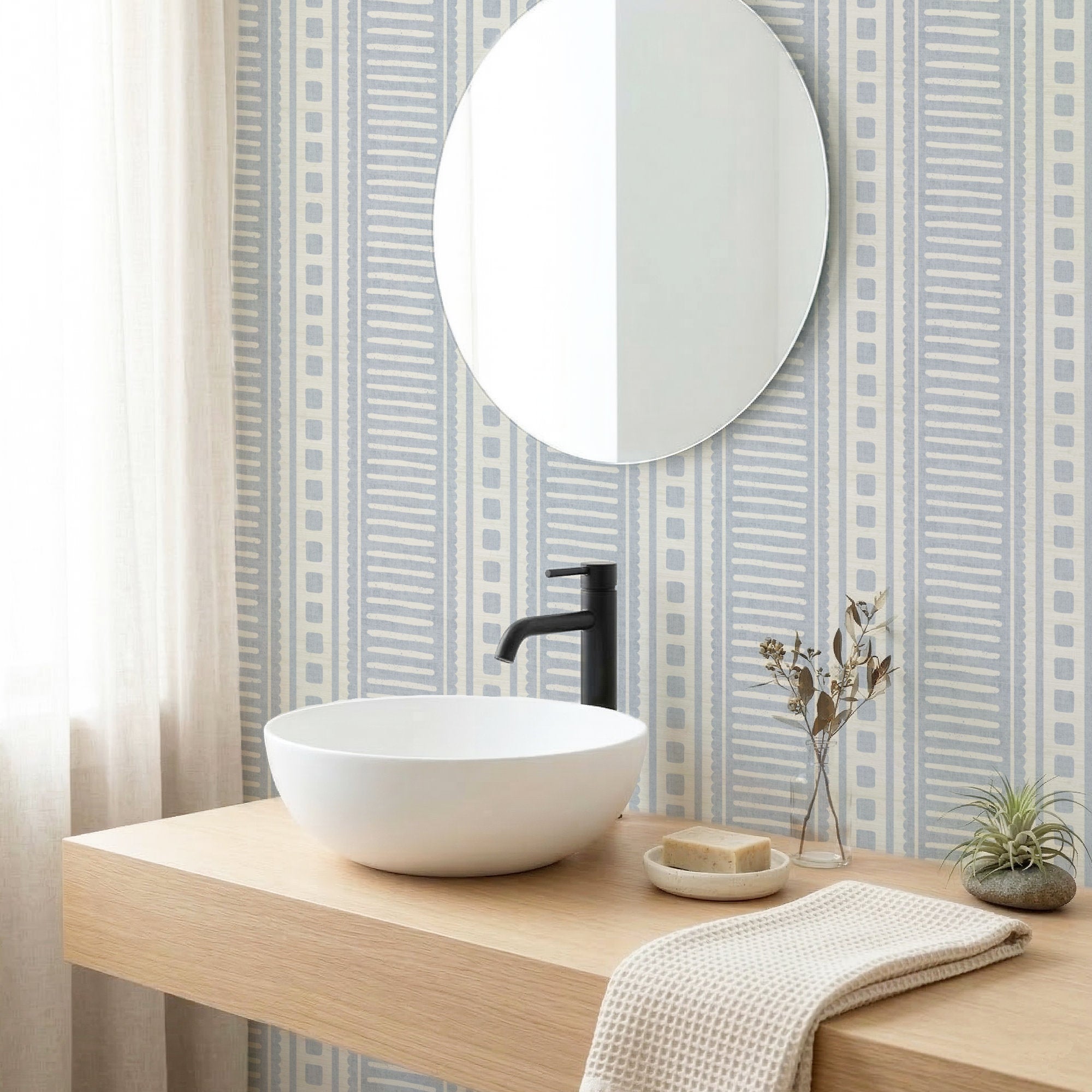 Cornflower blue coastal stripe wallpaper in a bathroom behind a round mirror and white basin on a wood vanity