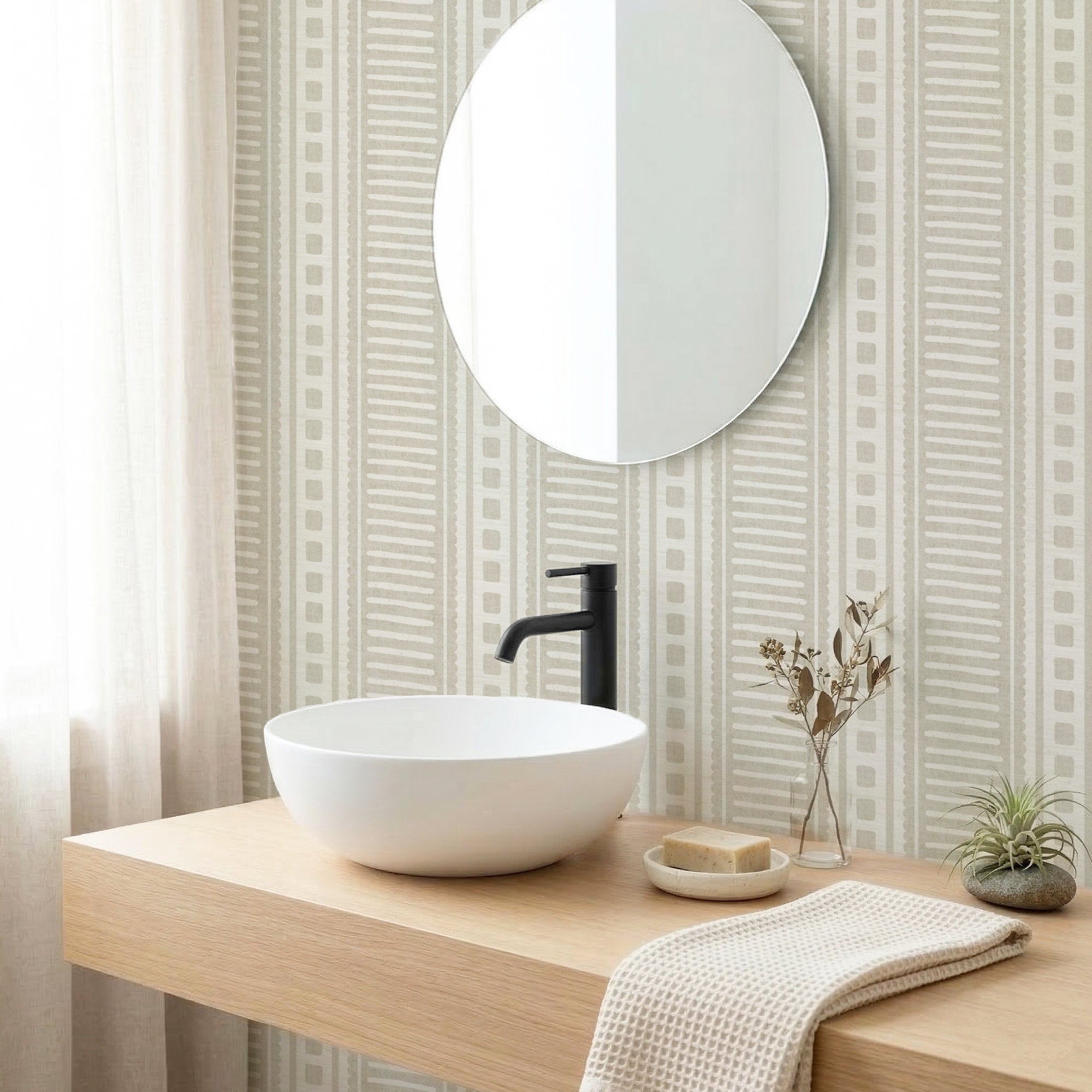Sandy beige coastal stripe wallpaper in a bathroom behind a round mirror and white vessel basin on a wood vanity