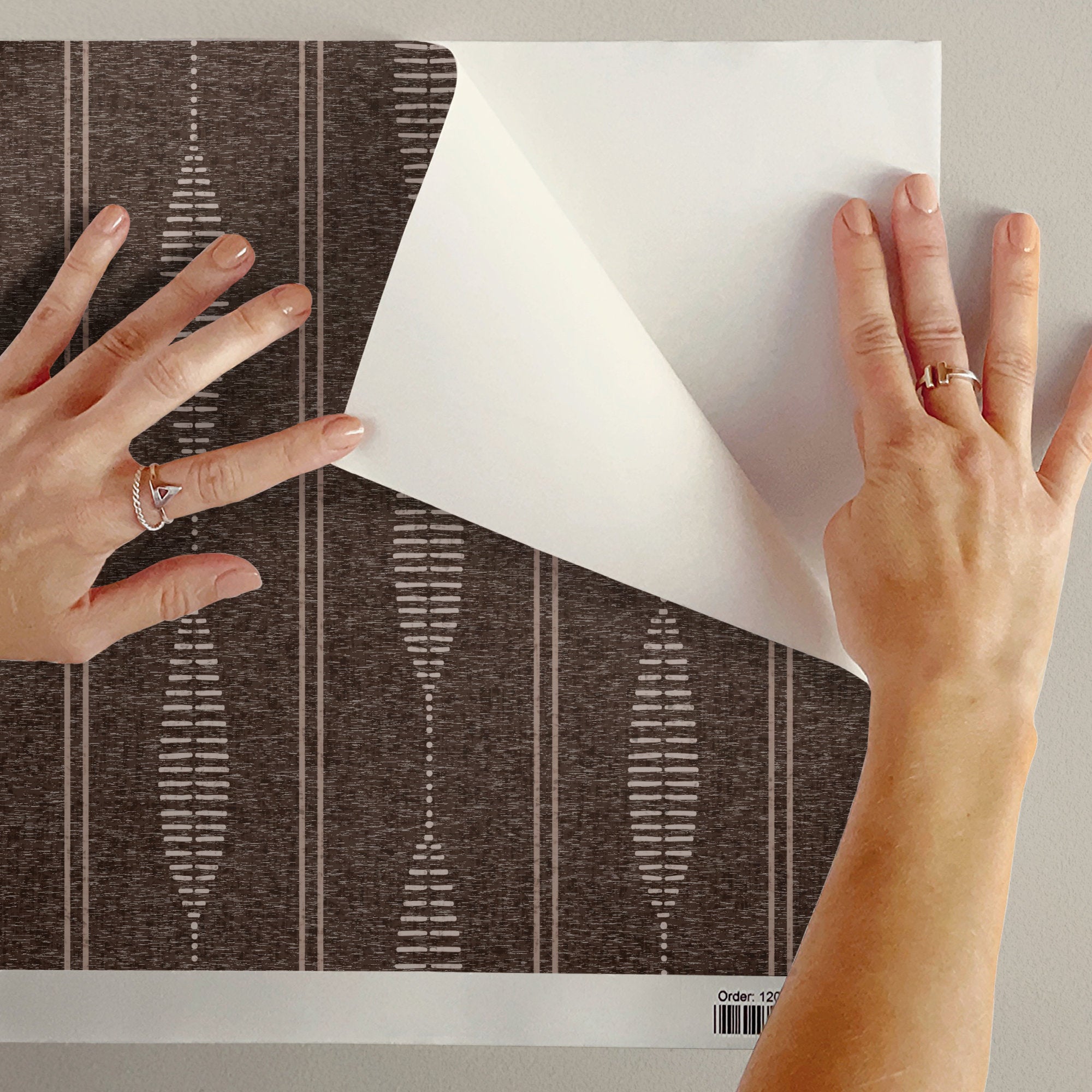 Peeling back brown linen stripe wallpaper to show the removable peel and stick finish