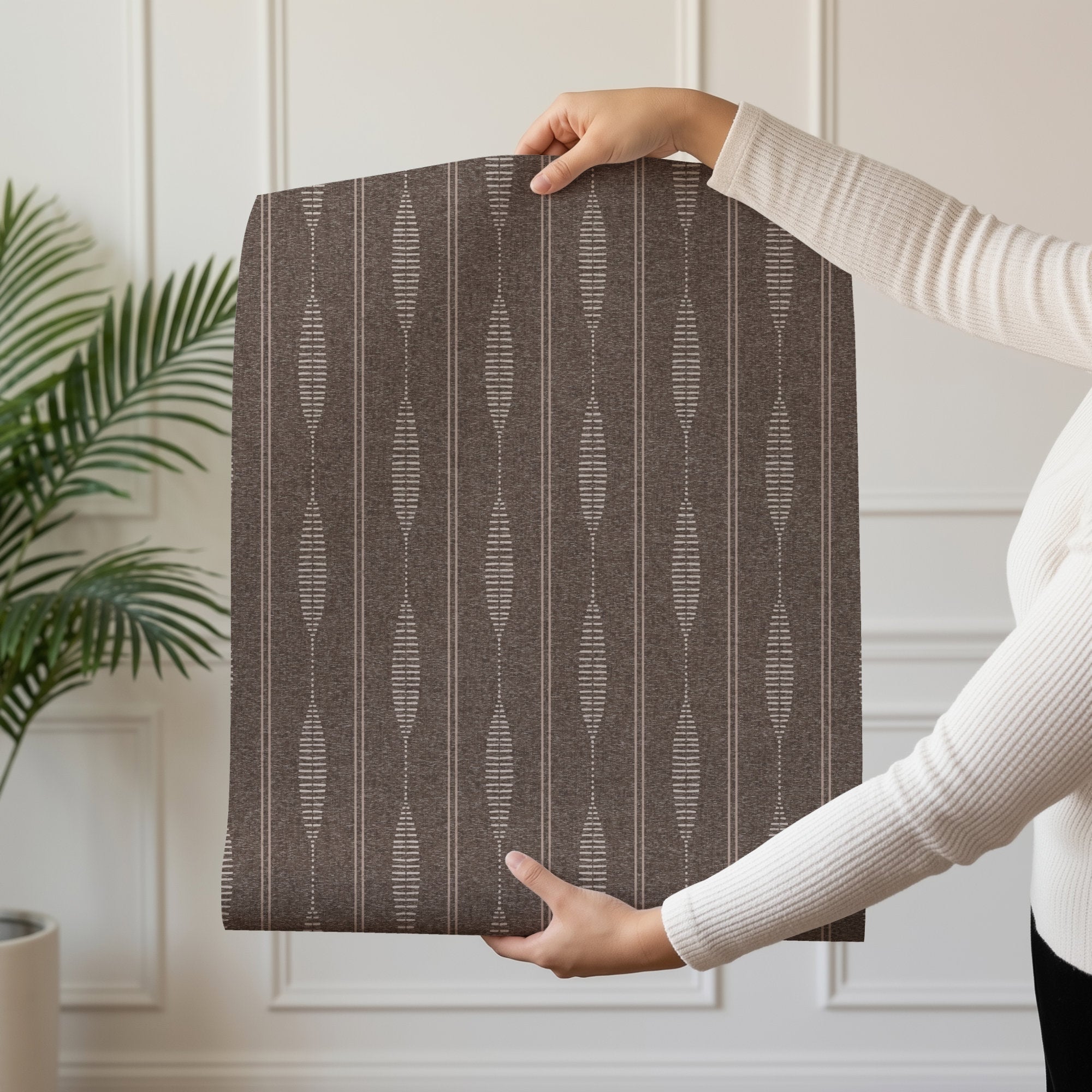 woman Holding a roll of brown linen stripe wallpaper to show the folk stripe pattern