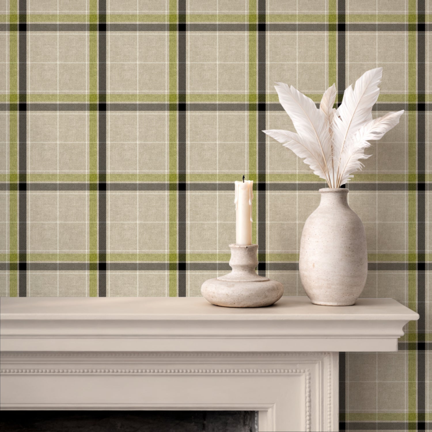 A styled interior scene showing a heritage plaid wallpaper pattern in beige, olive green, and black behind a white mantel with a candle holder and a vase of white feathers.