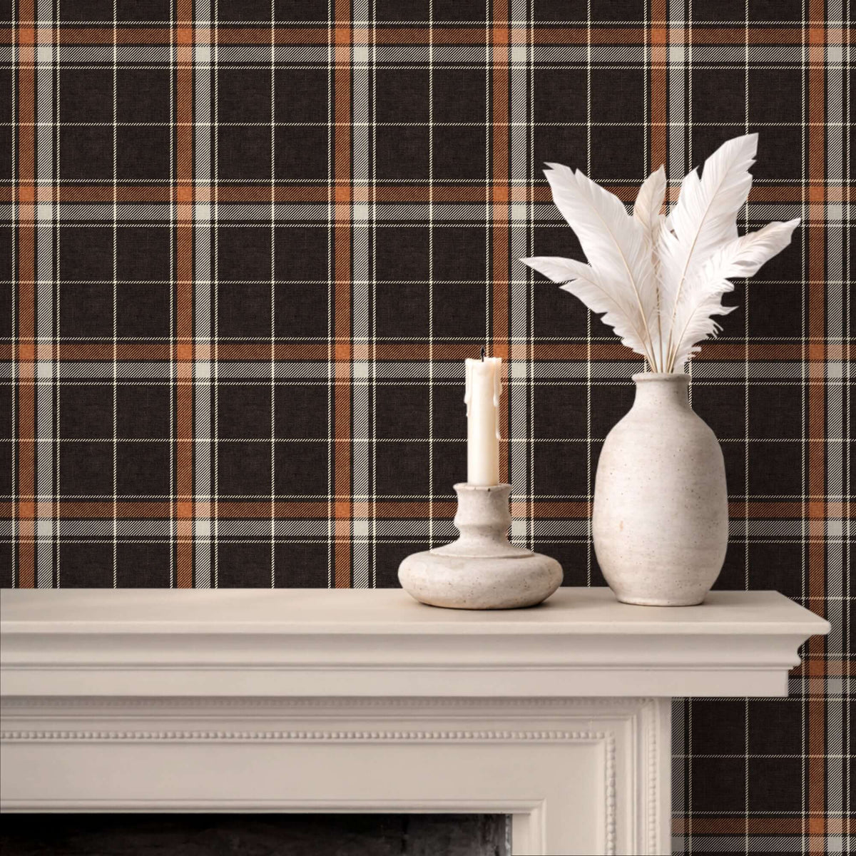 Brown and orange heritage plaid wallpaper displayed behind a white mantel with a candle holder and a vase of white feathers.