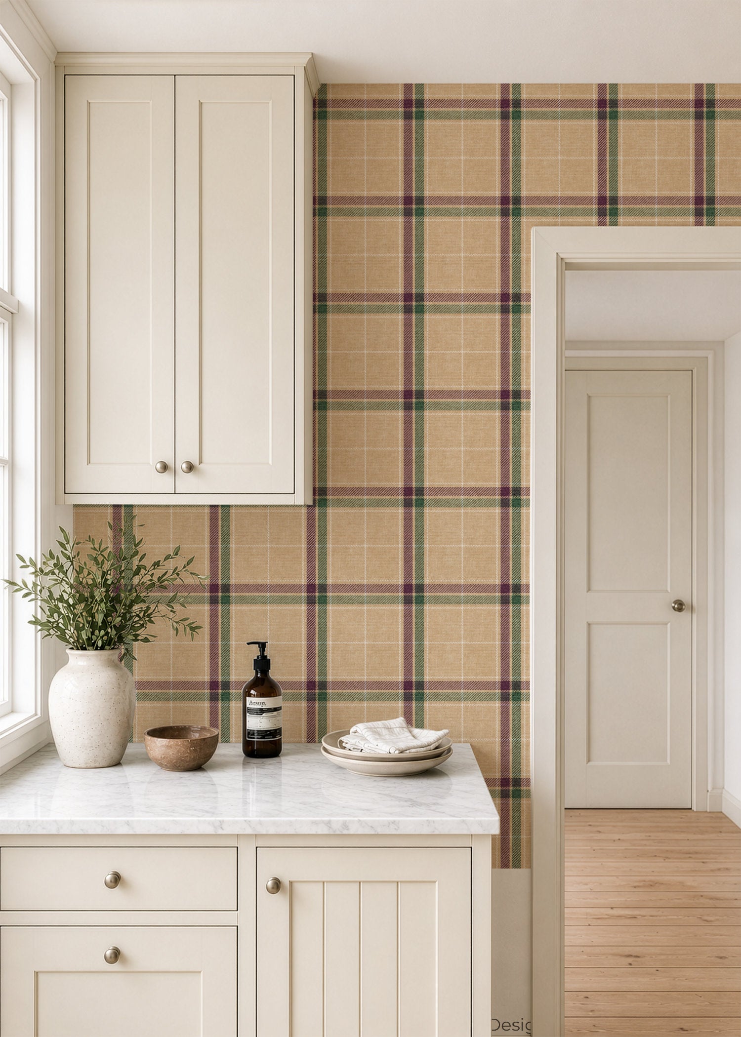 A styled kitchen interior featuring a beige heritage plaid wallpaper accent wall behind cream-colored cabinets and a marble countertop. The plaid pattern has intersecting stripes of green, red, and dark brown on a warm beige background.