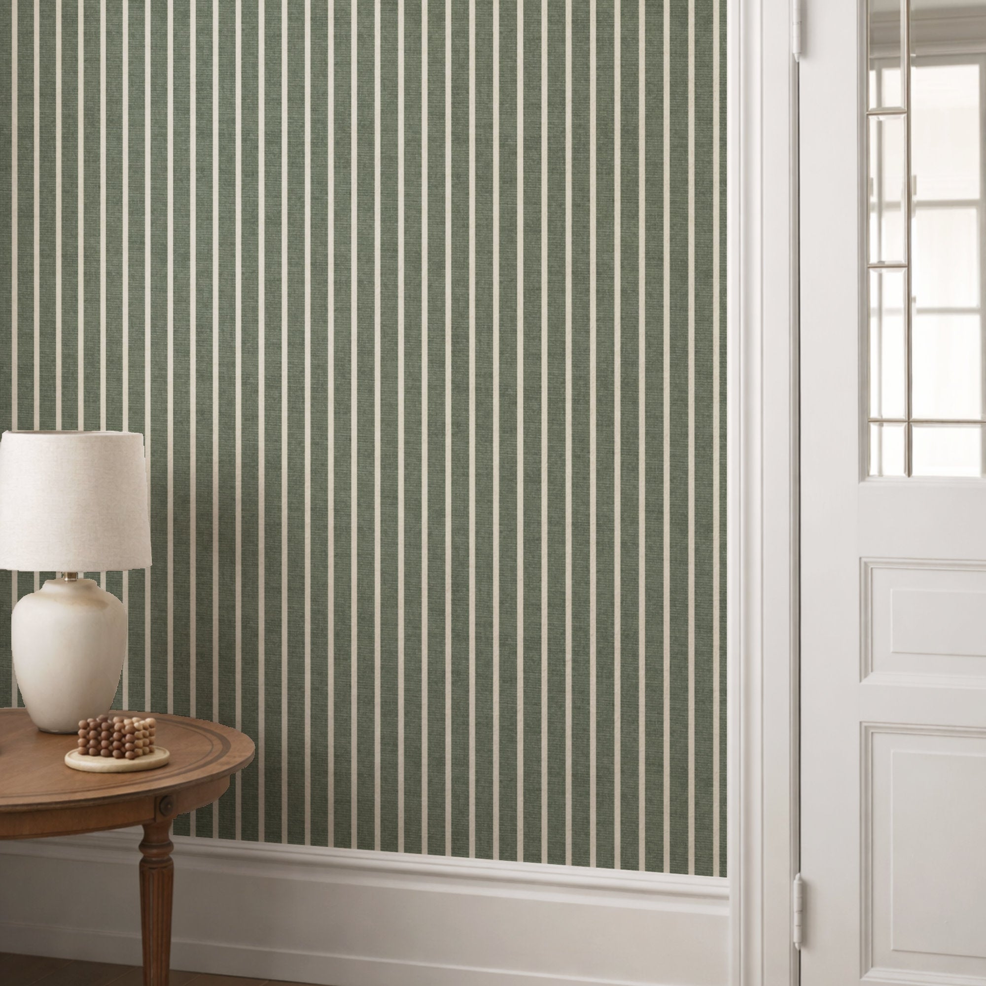 Olive green pinstripe wallpaper in a hallway behind a round console table with a cream lamp