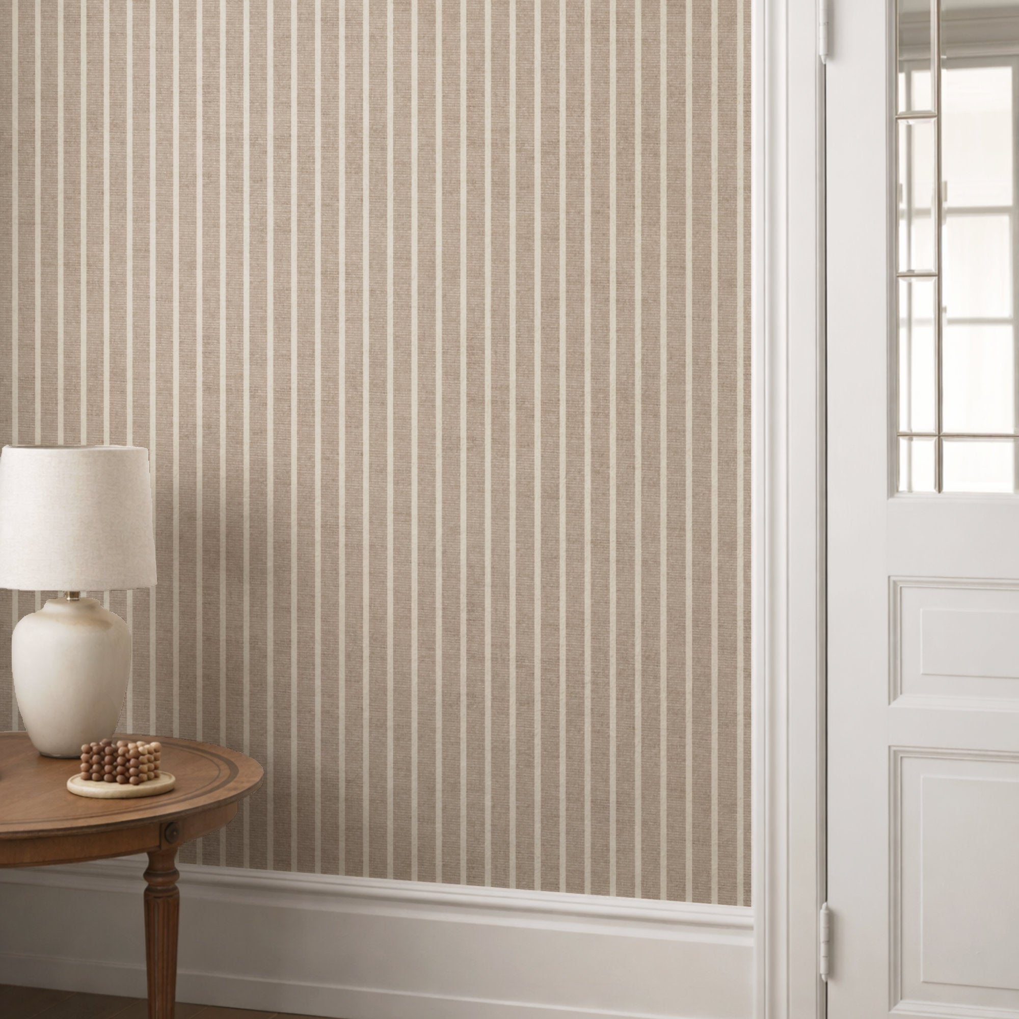 Warm beige pinstripe wallpaper in a hallway behind a round console table with a cream lamp