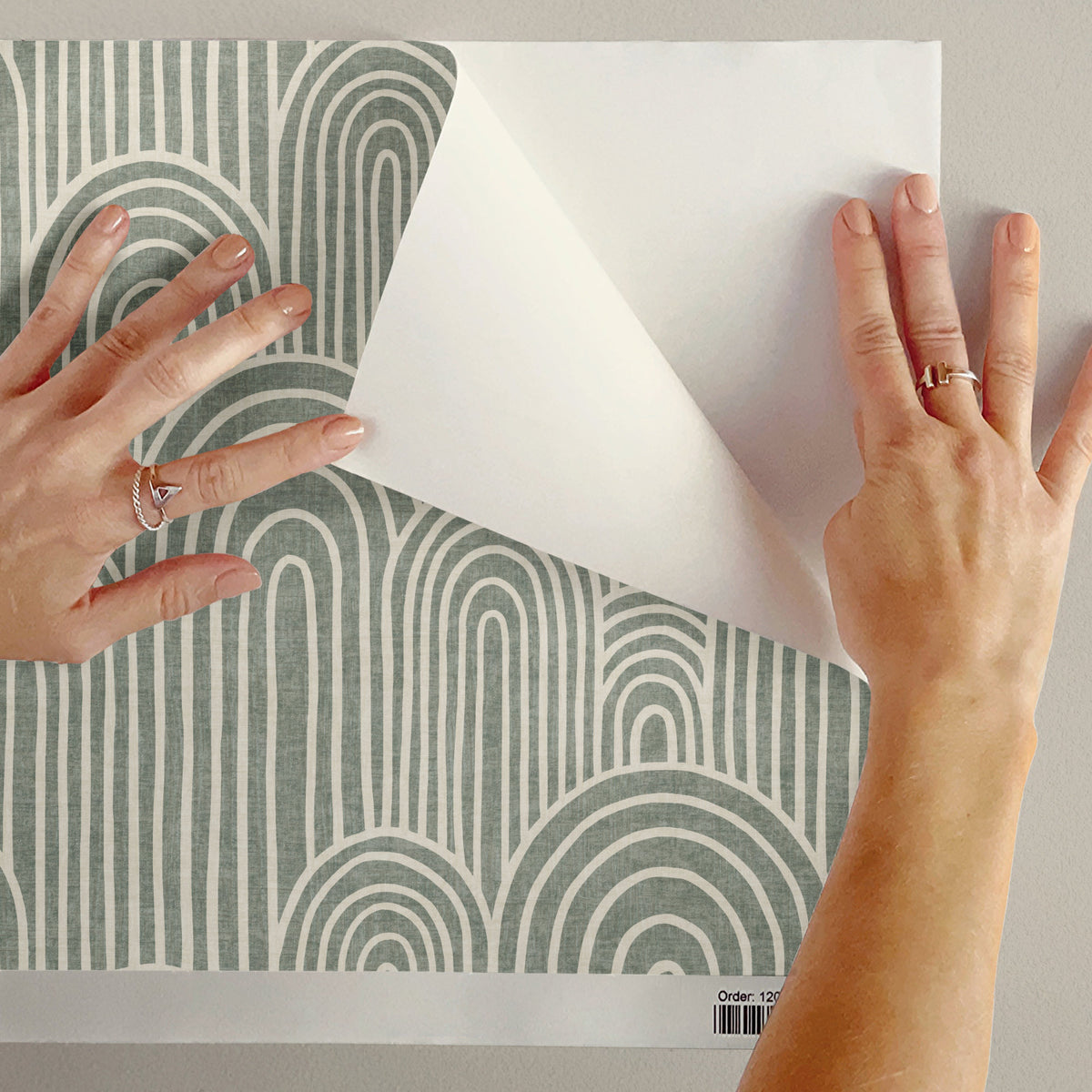 Arches peel and stick wallpaper sample in sage green being peeled showing adhesive backing