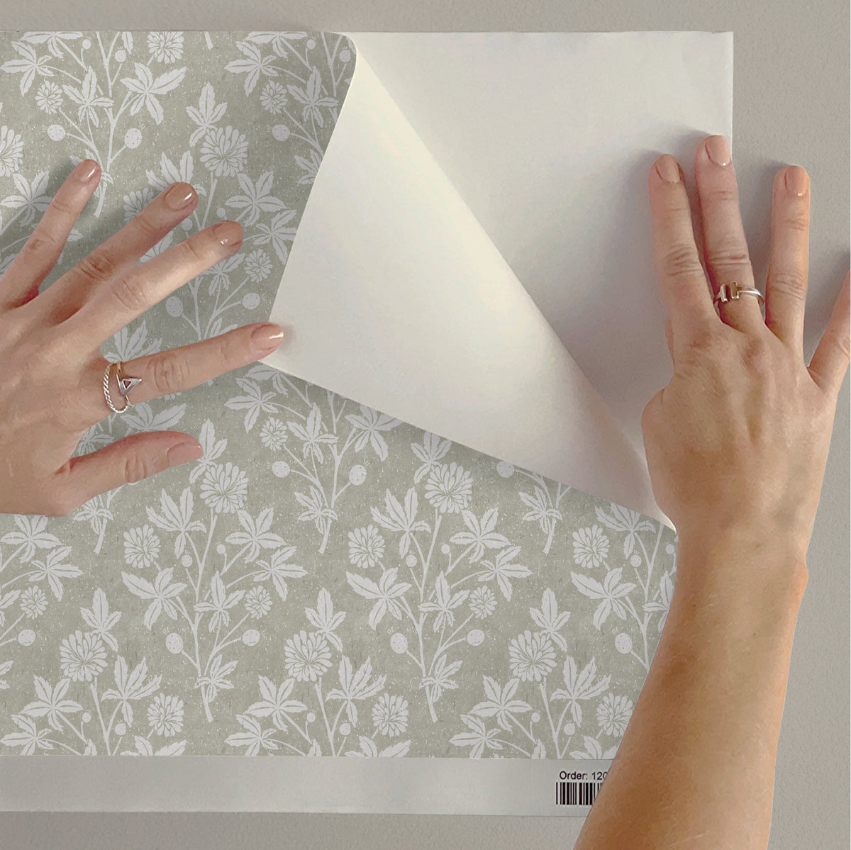 Person applying a peel and stick floral wallpaper design to a wall.