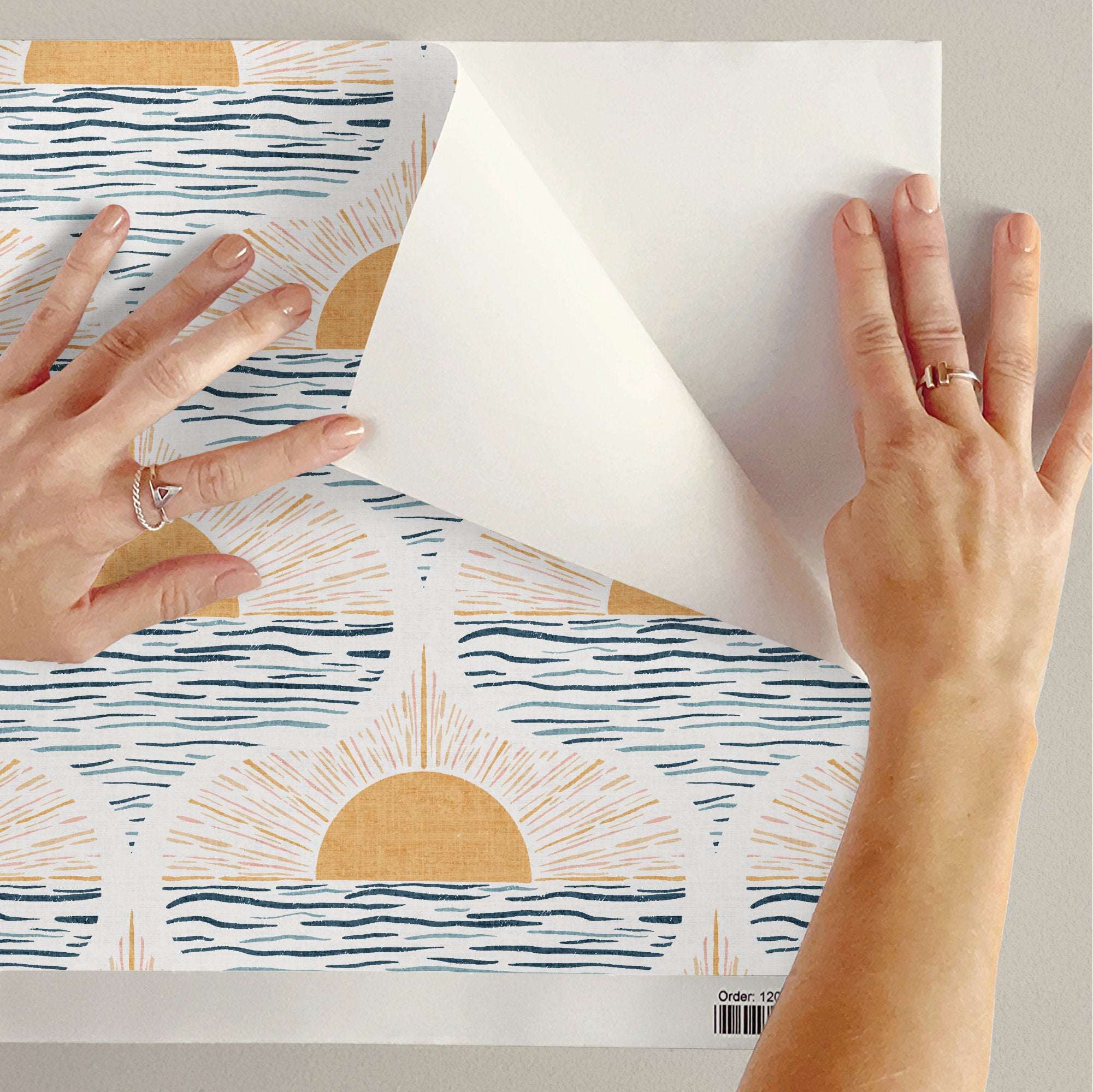 Wallpaper sheet with cream background, blue waves, and golden sun circles, being applied