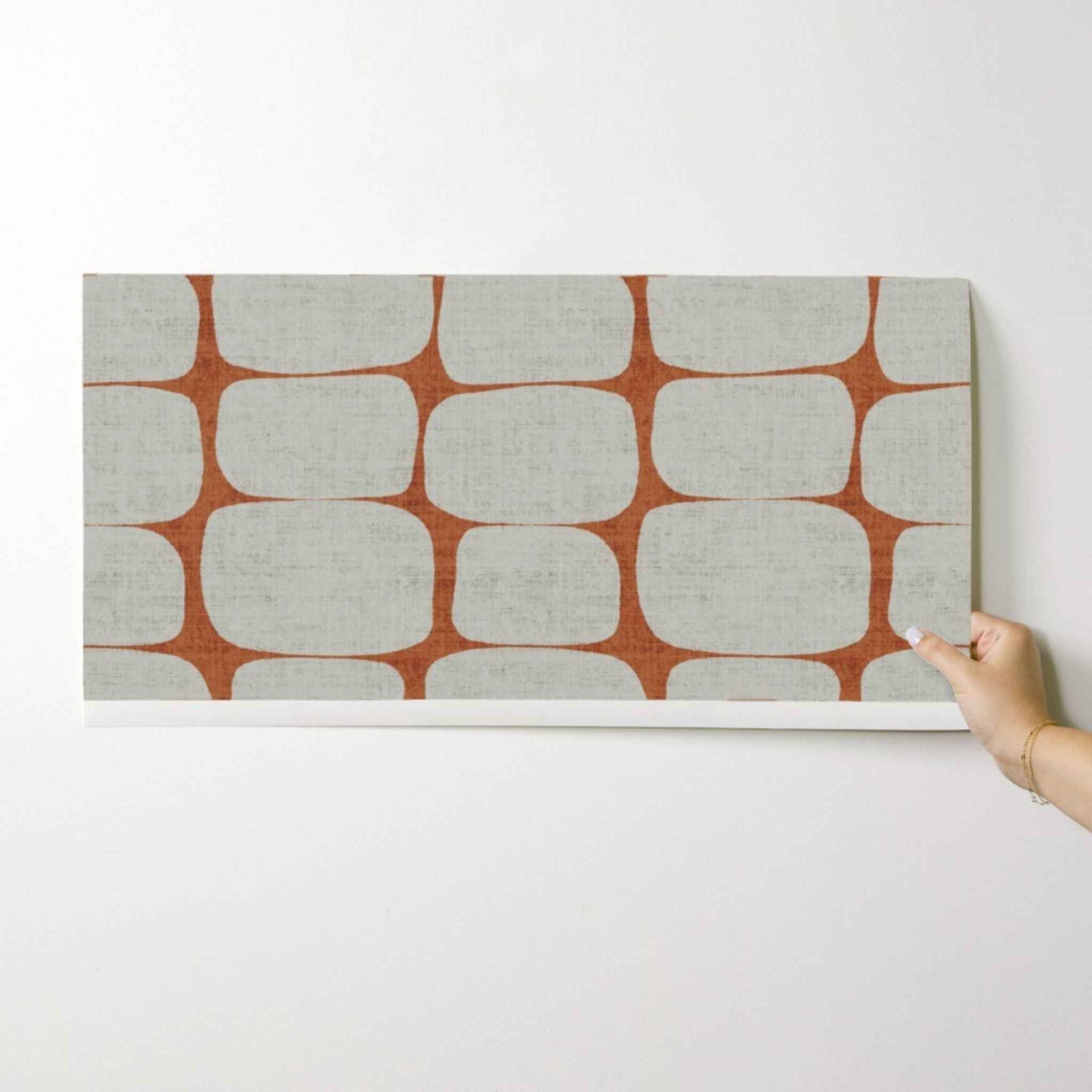 Hand holding a sample of retro geometric stripe wallpaper in terracotta and cream.