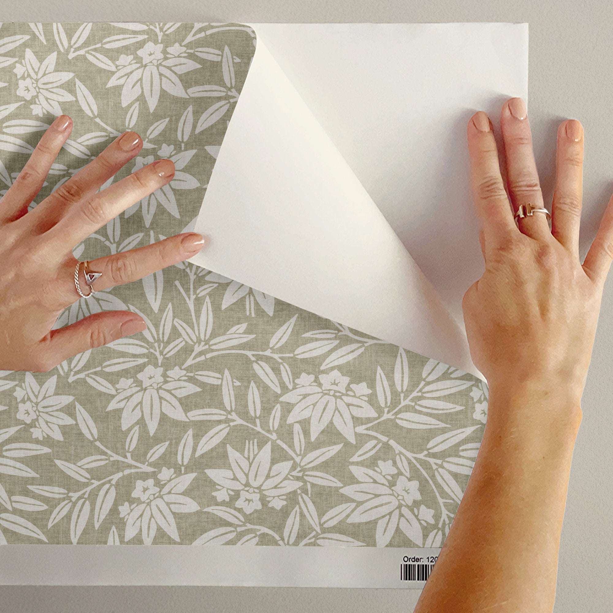 Botanical wallpaper sheet held for installation, showing cream leaf pattern on gray base