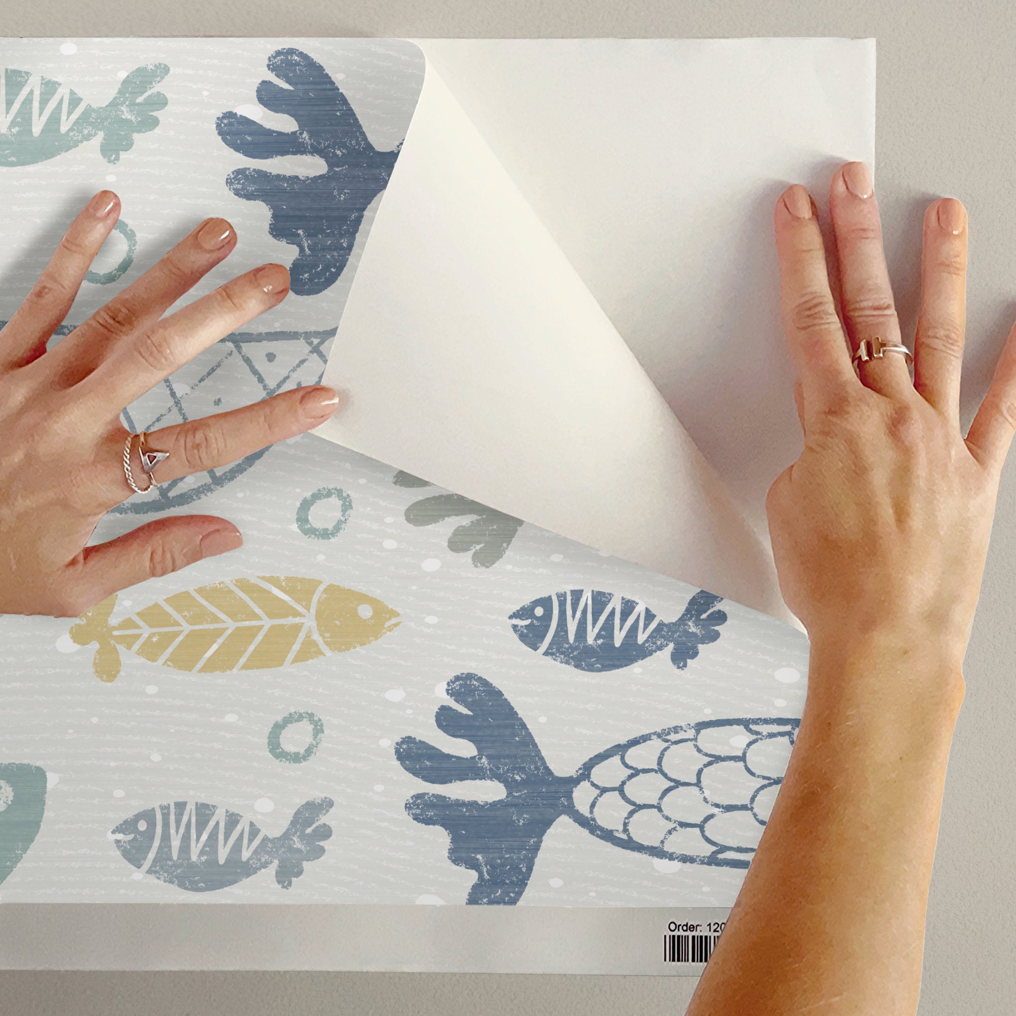 A peel and stick sample of multicolour school of fish wallpaper, showing the hand-drawn fish pattern in blue, green, grey and mustard on cream.