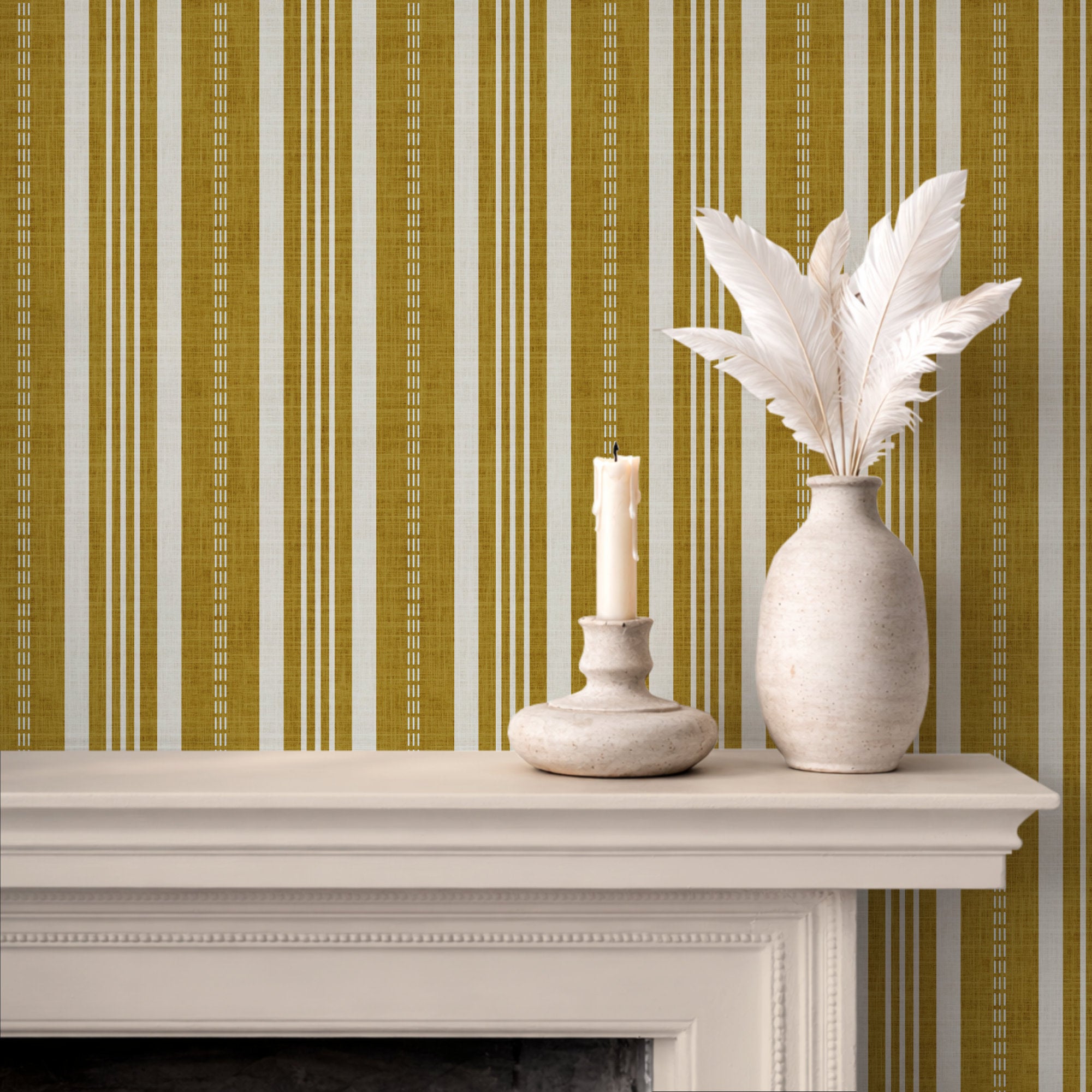Vertical ticking stripe wallpaper in mustard yellow and cream, styled behind a white fireplace mantel with a textured vase of white feathers and a candle holder.