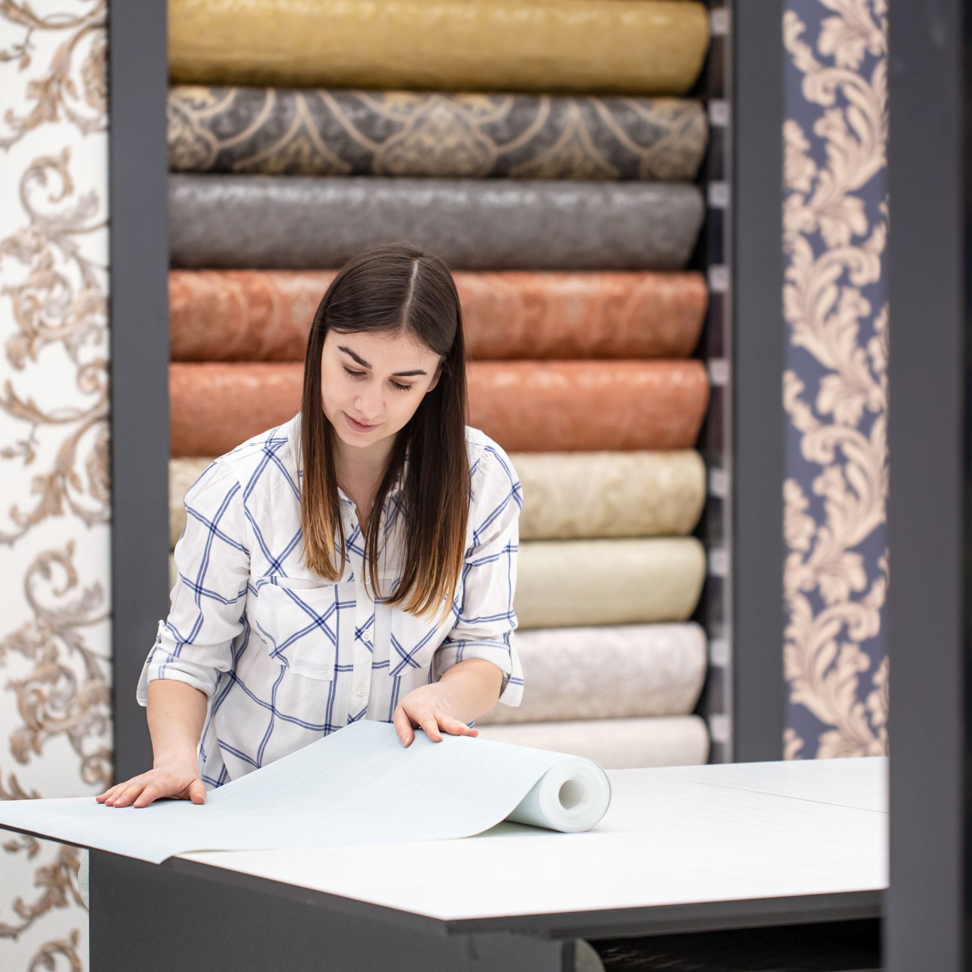 A woman selecting wallpaper rolls in a store while learning how to choose wallpaper.