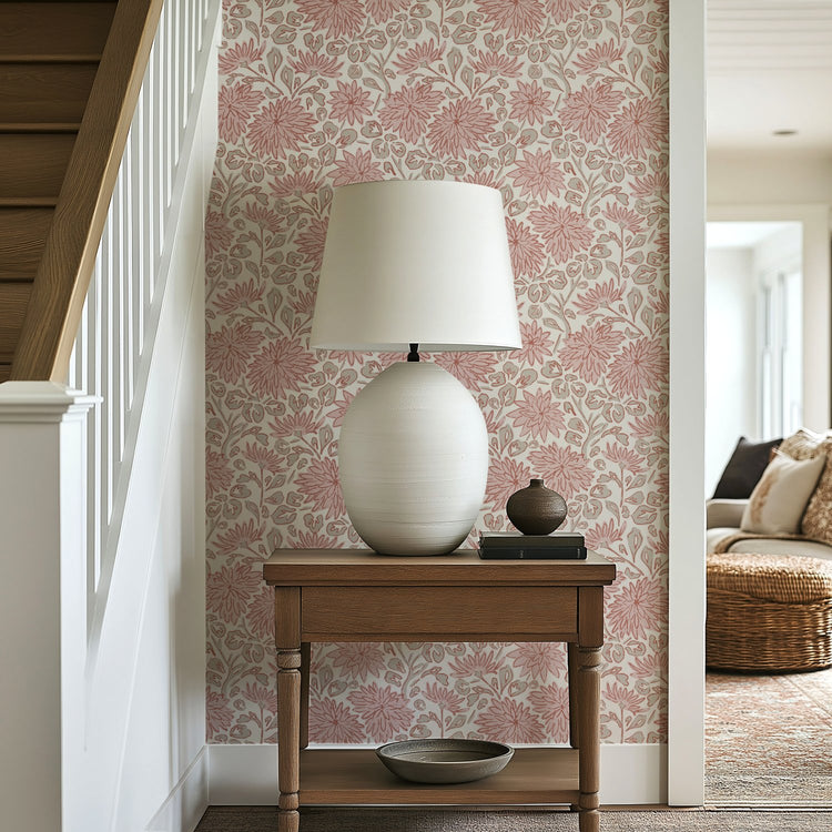 Pink floral wallpaper in a hallway with wooden side table, ceramic lamp, and staircase.