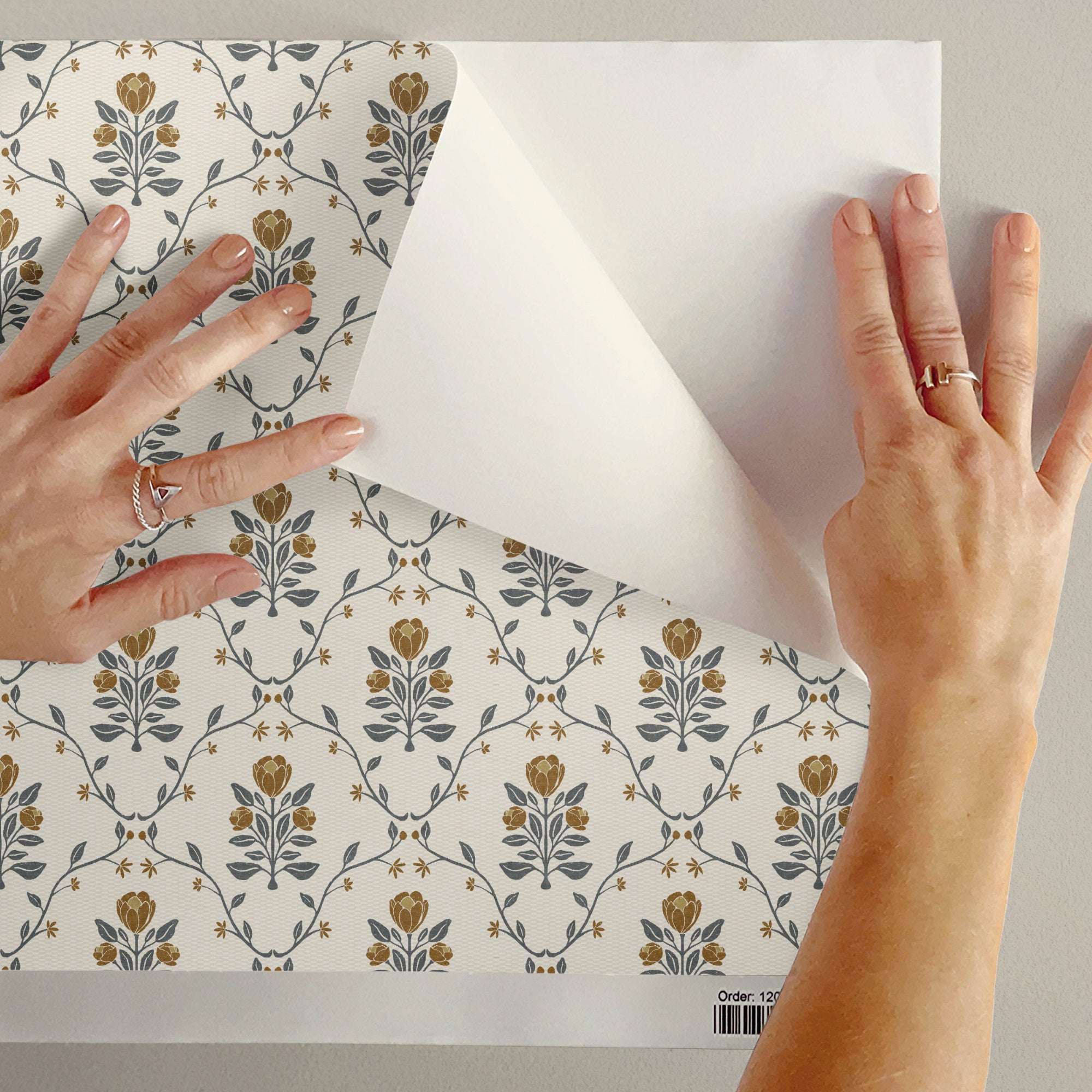 Wallpaper backing being peeled off; cream botanical trellis pattern with blue-gray leaves and tan blooms
