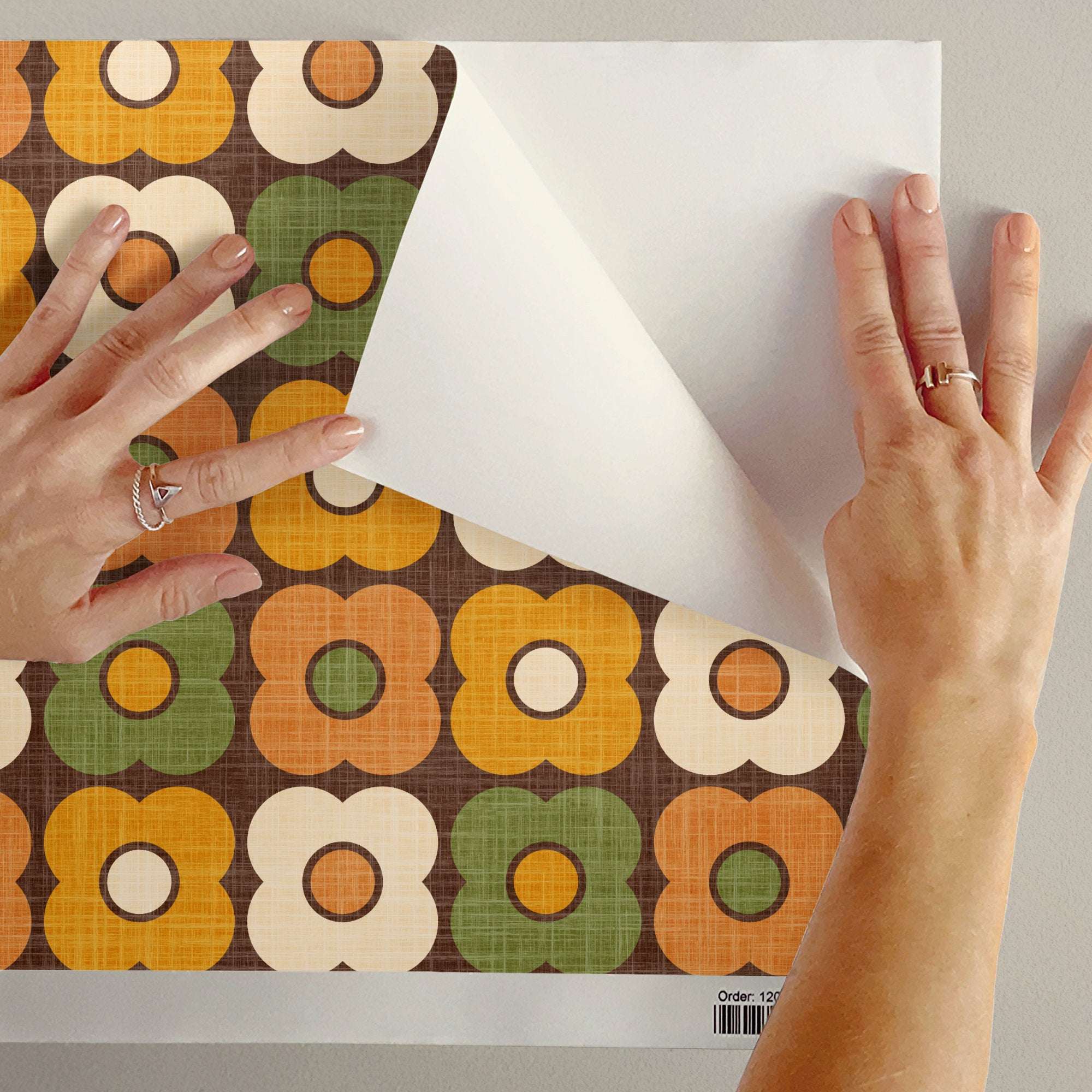Retro daisy circle pattern wallpaper sheet being applied; green, orange and white flower motifs.