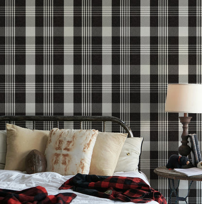Black checkered wallpaper with a bold plaid design as a bedroom feature wall, styled with layered neutral pillows and cosy bedding