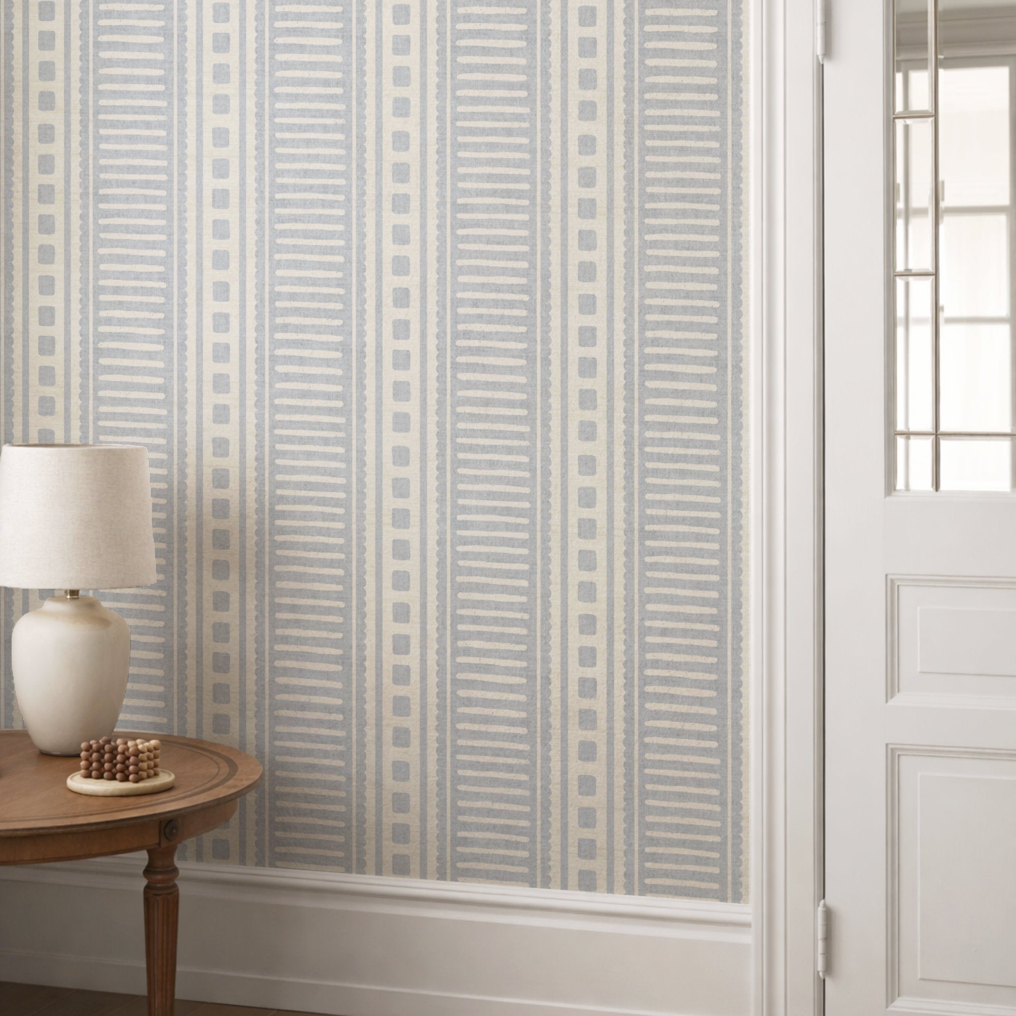 Cornflower blue coastal stripe wallpaper in a hallway behind a console table with a cream lamp