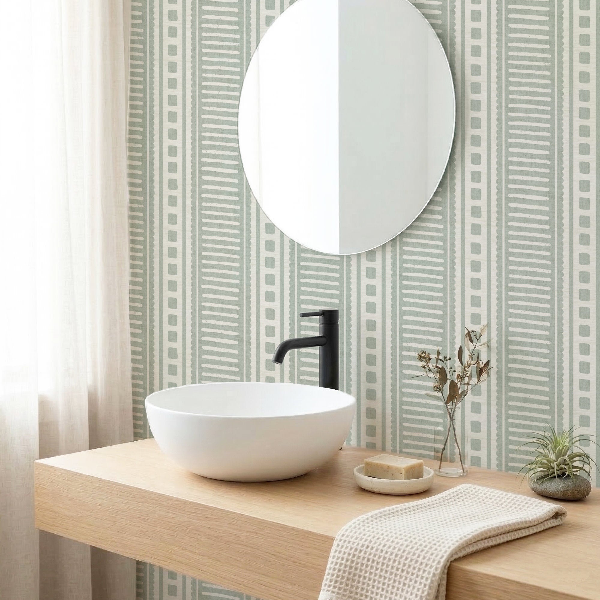 Sage green coastal stripe wallpaper in a bathroom behind a round mirror and white basin with a black tap