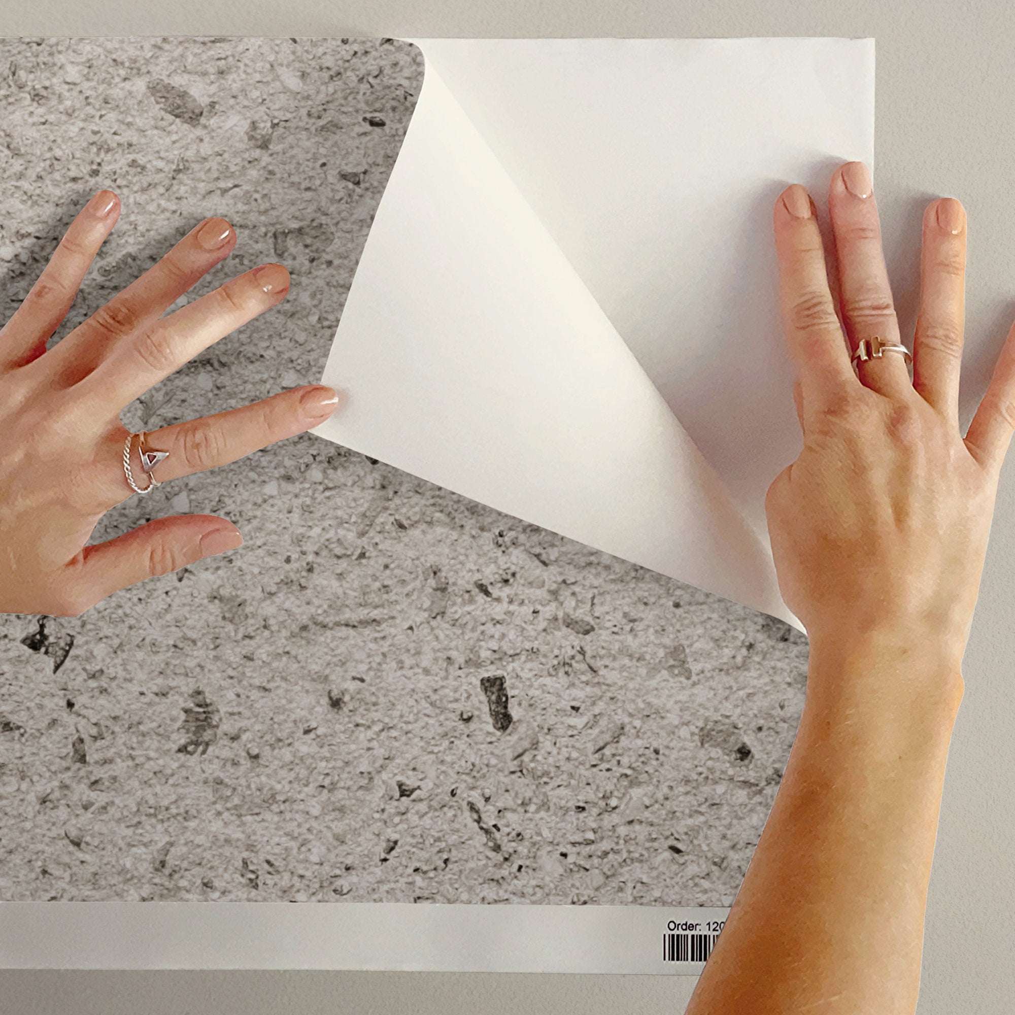Concrete-effect wallpaper sample held by hands, light grey speckled concrete pattern