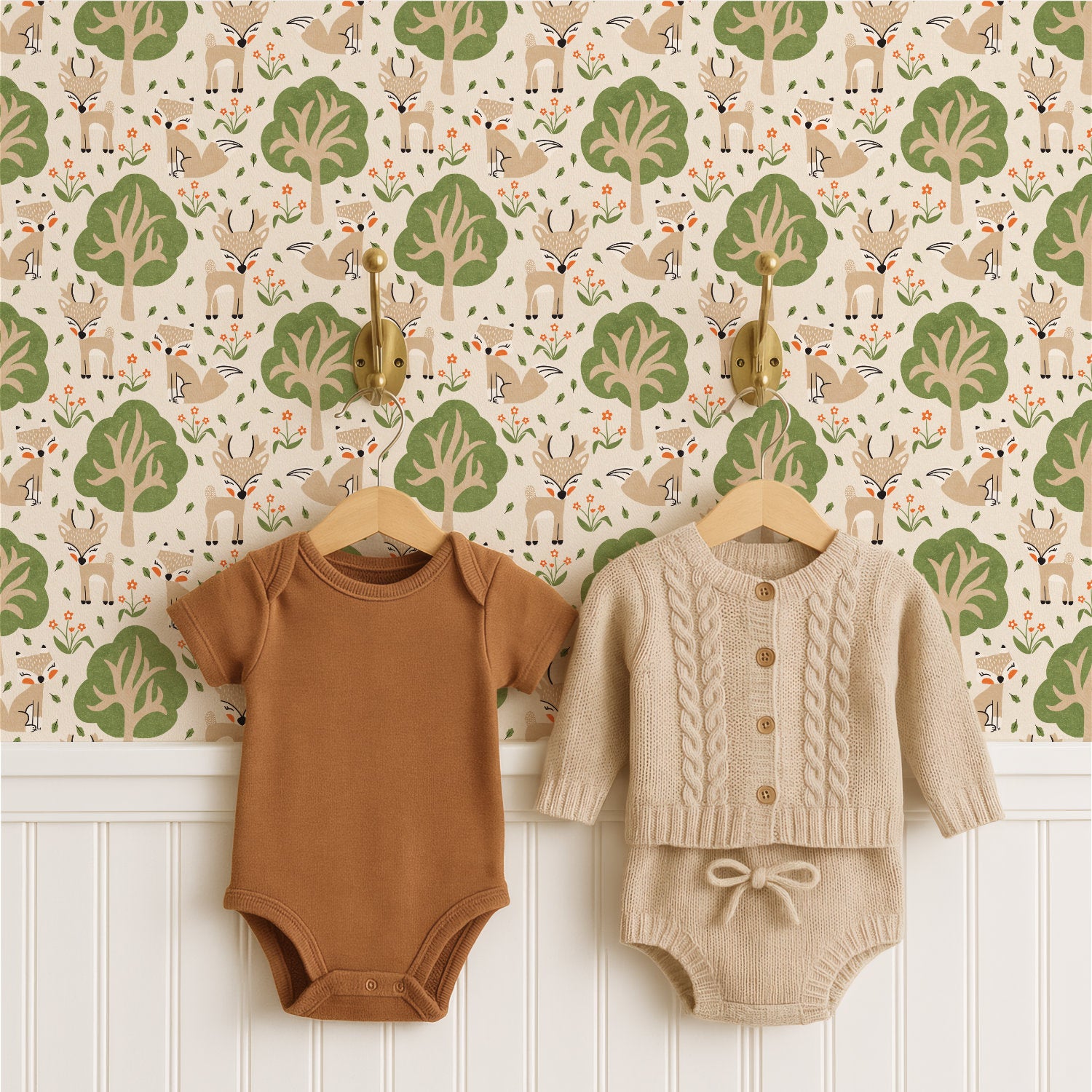 Two baby clothing sets hang on wooden hangers against a woodland nursery wallpaper pattern. On the left is a short-sleeve brown bodysuit, and on the right is a cream cable-knit button-front romper with matching bow detail.