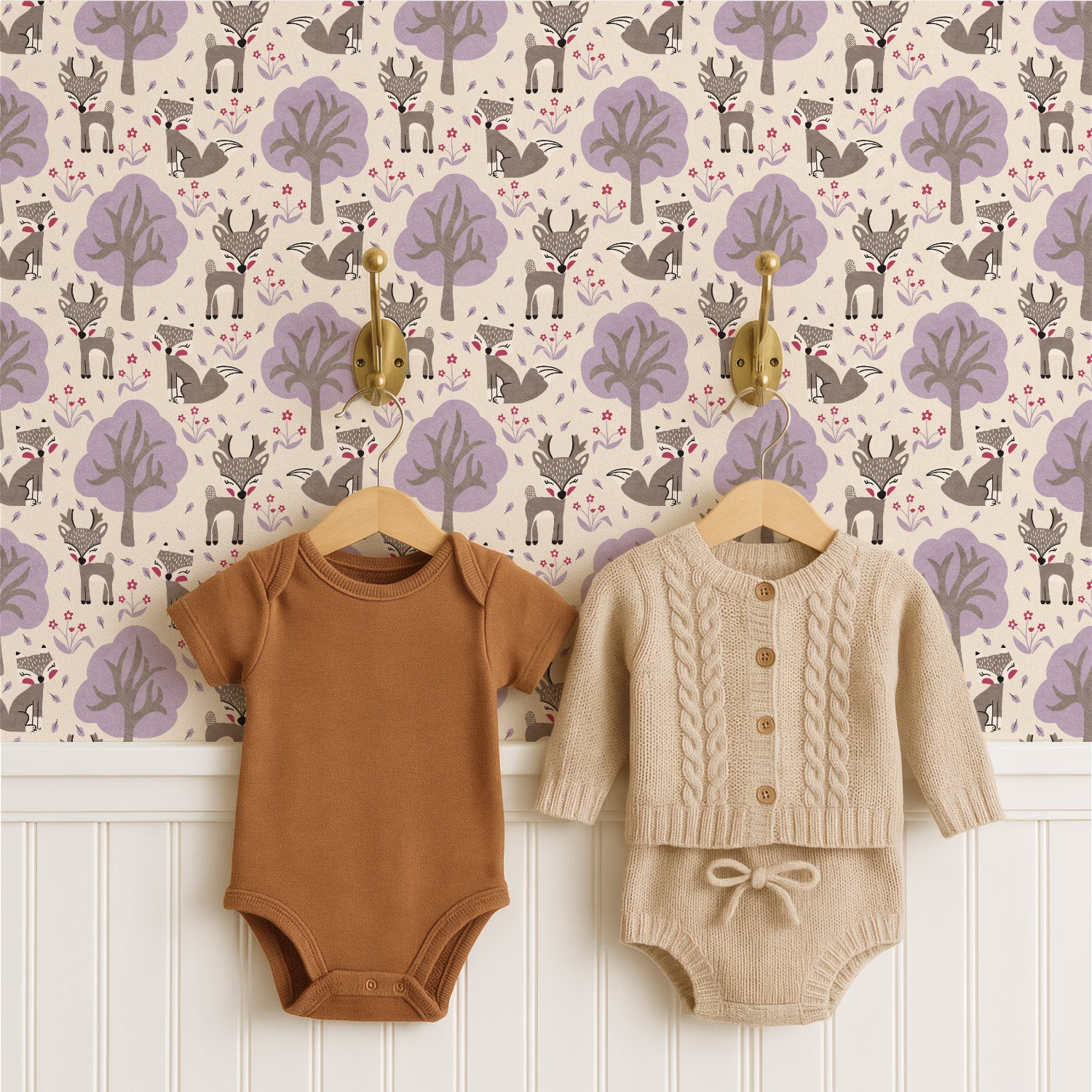 Two baby bodysuits hanging on wooden hangers against a woodland nursery wallpaper pattern background. The left bodysuit is a solid warm brown short-sleeve one-piece.