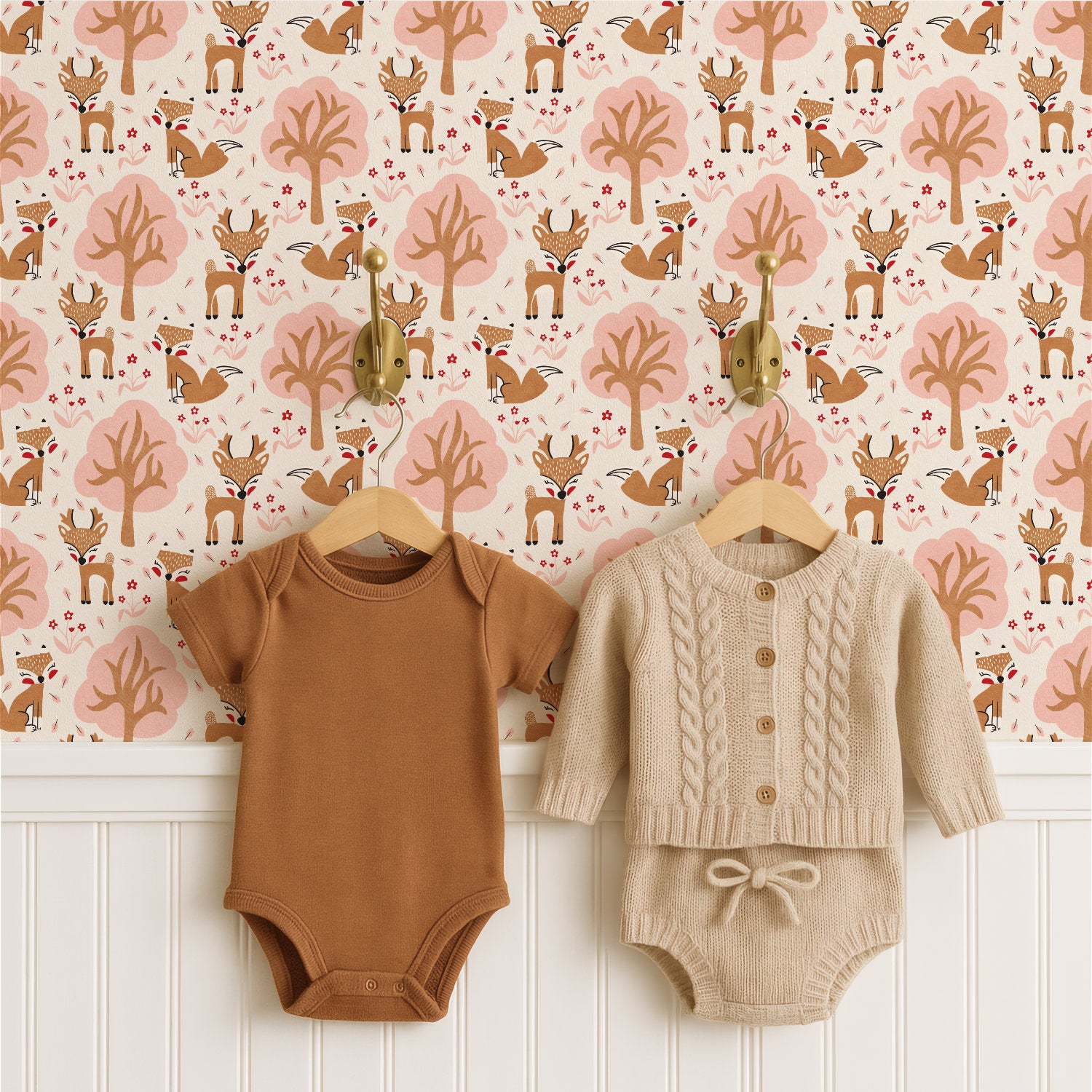 Two baby bodysuits hanging on wooden hangers against a woodland nursery wallpaper pattern background. The left bodysuit is a solid warm brown short-sleeve one-piece.