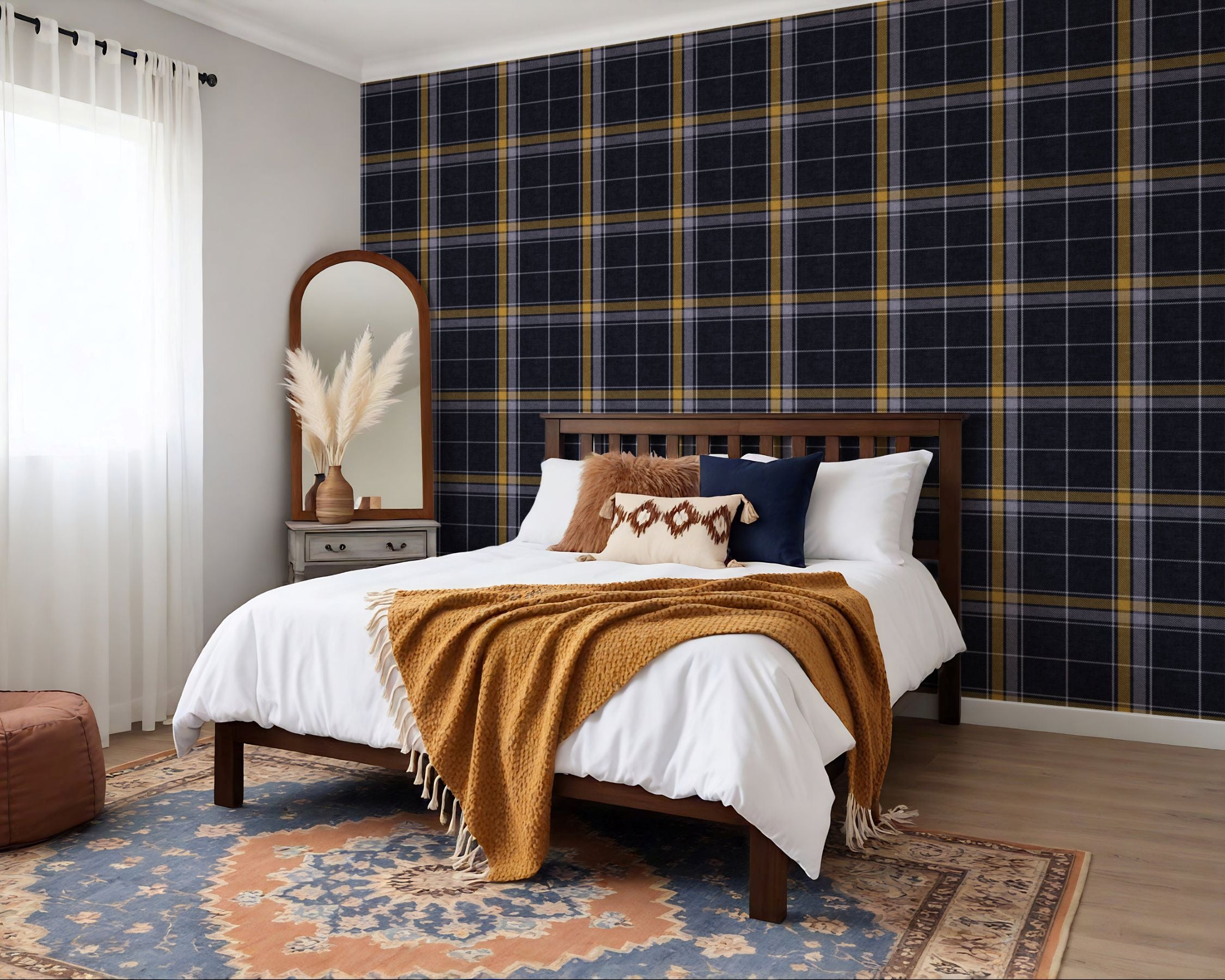A styled bedroom featuring a bold navy blue and yellow heritage plaid wallpaper accent wall behind a wooden bed with white bedding and a mustard throw blanket.
