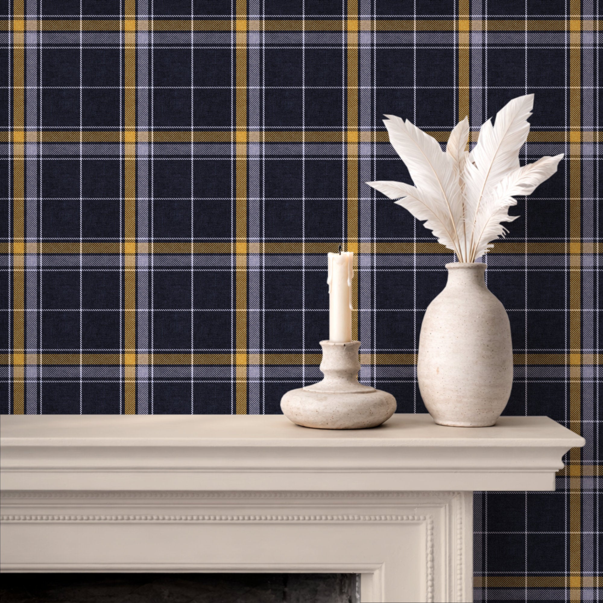 A styled interior scene showing a cream mantel with a candle holder and a vase of white feathers in front of a navy, yellow, and white heritage plaid wallpaper