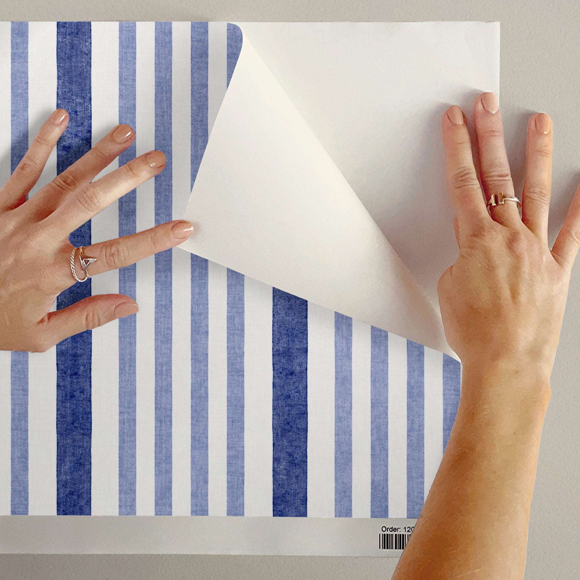 Person aligning a wallpaper sheet with vertical watercolor-style stripes in dark blue and off-white