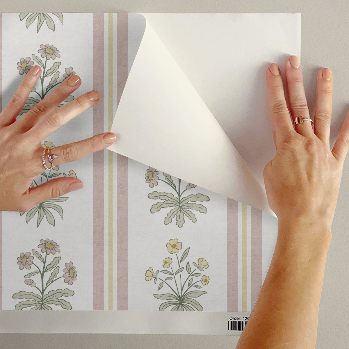Floral stripe peel and stick wallpaper sample in pink being peeled showing adhesive backing
