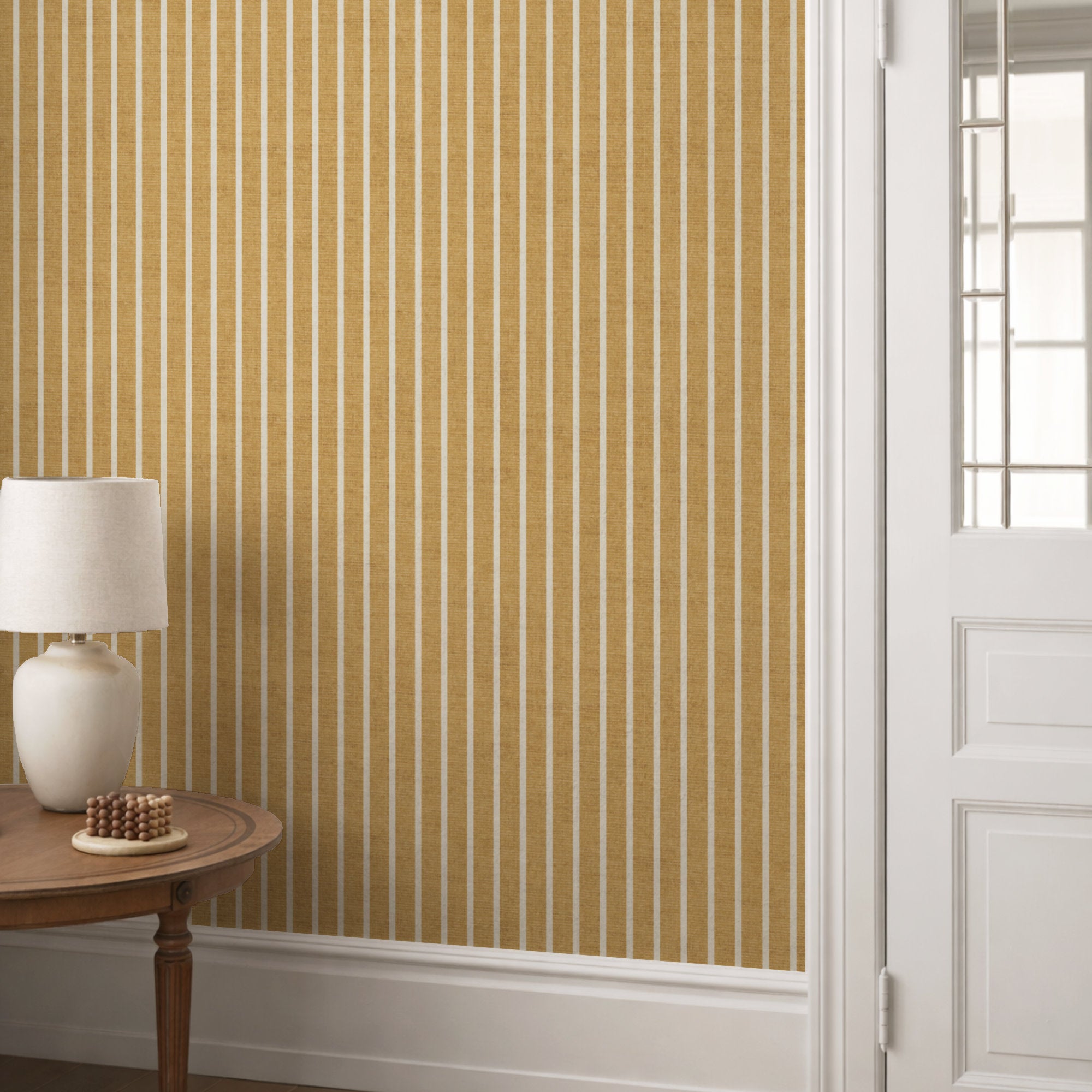 Mustard yellow pinstripe wallpaper in a hallway behind a round console table with a cream lamp