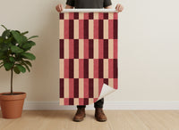 Retro block stripe wallpaper roll in burgundy colourway being held to show scale