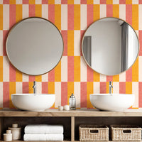 Retro block stripe wallpaper in coral pink and amber orange in bathroom with round mirrors
