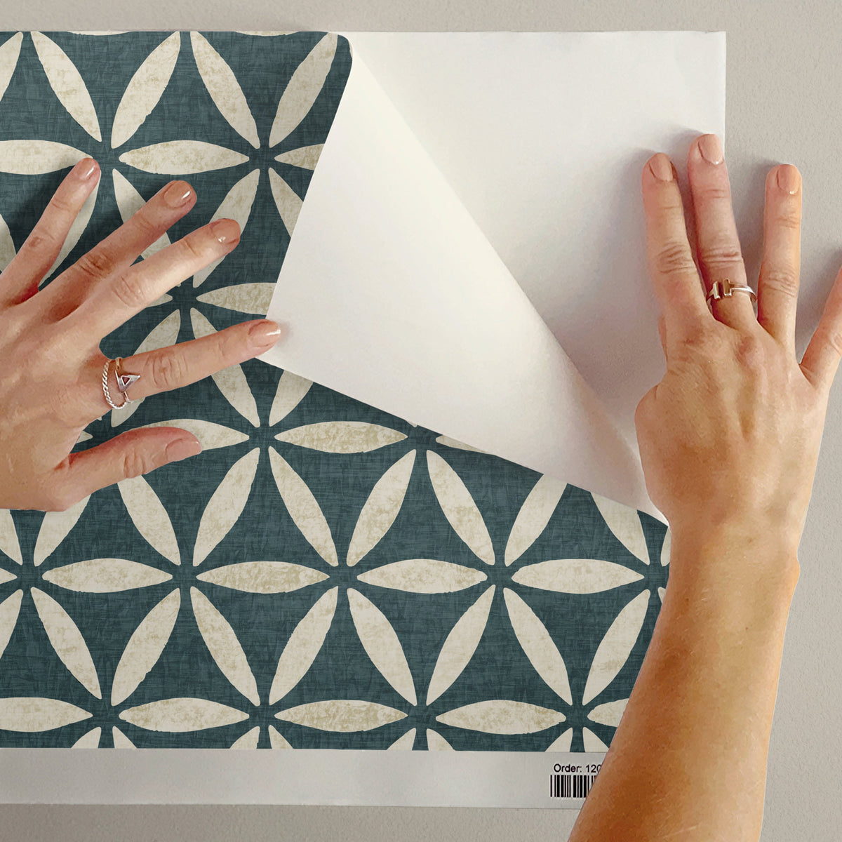 Sacred geometric peel and stick wallpaper sample in teal blue being peeled showing adhesive backing