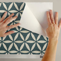 Sacred geometric peel and stick wallpaper sample in teal blue being peeled showing adhesive backing