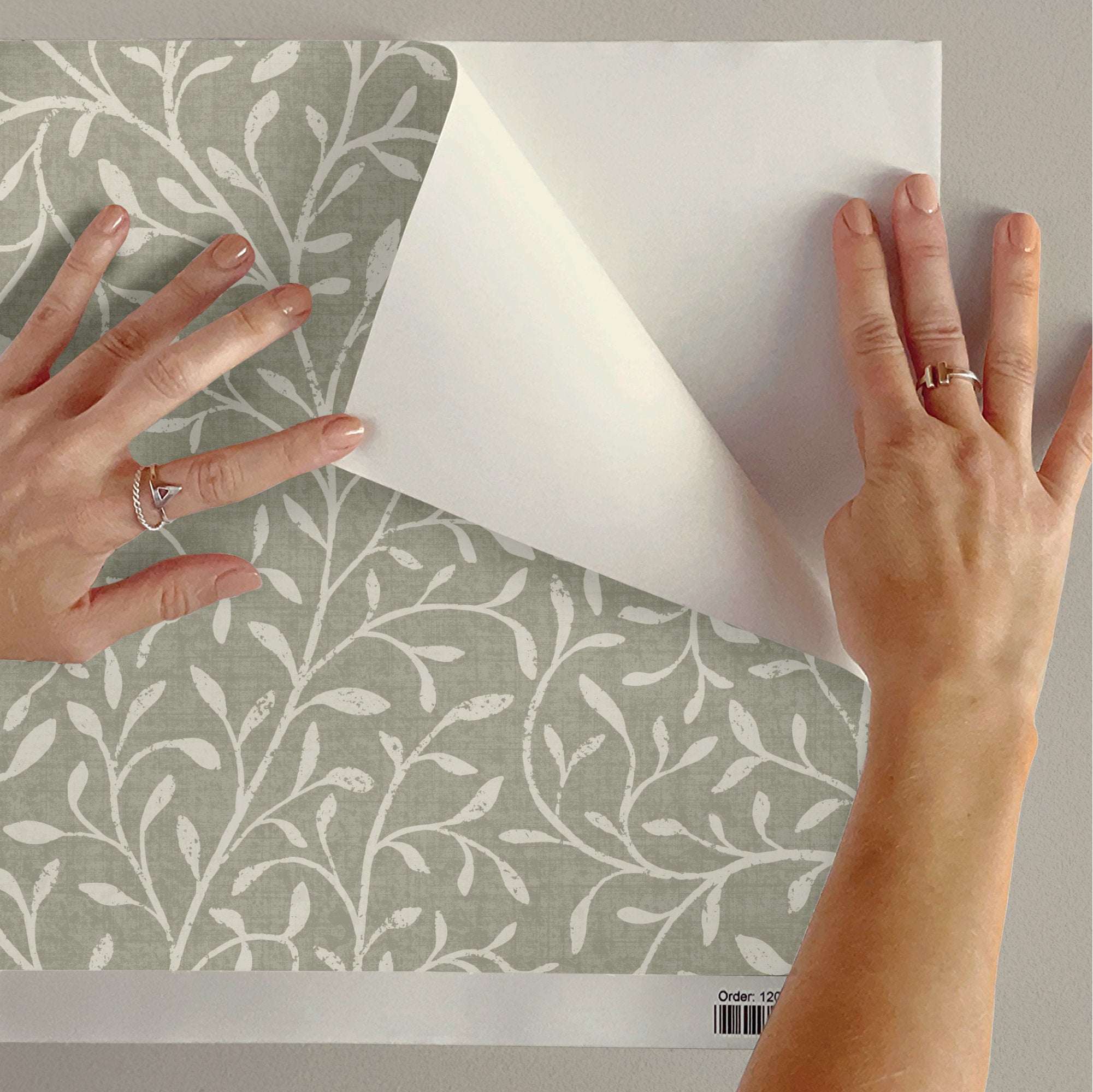 Hands smoothing botanical leaf silhouette wallpaper with white vine pattern on gray wall