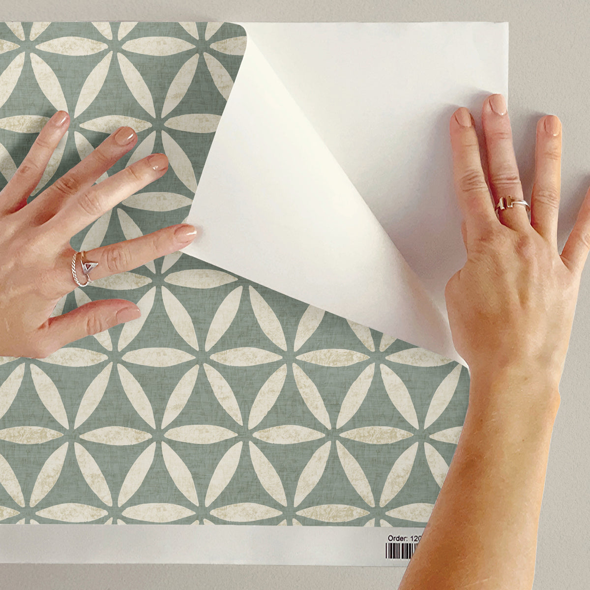 Person holding a sample of green geometric wallpaper with flower of life circles