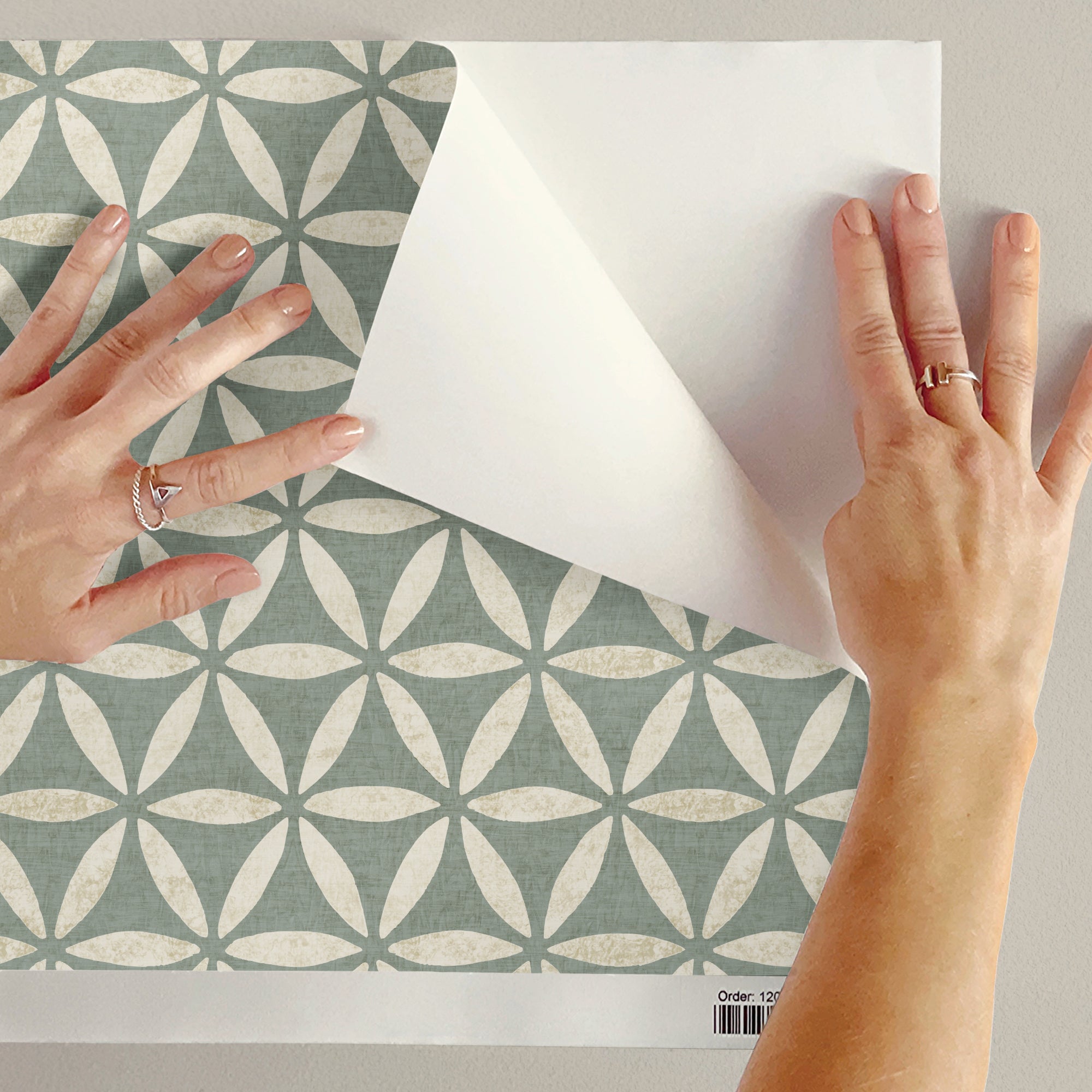 Person holding a sample of green geometric wallpaper with flower of life circles