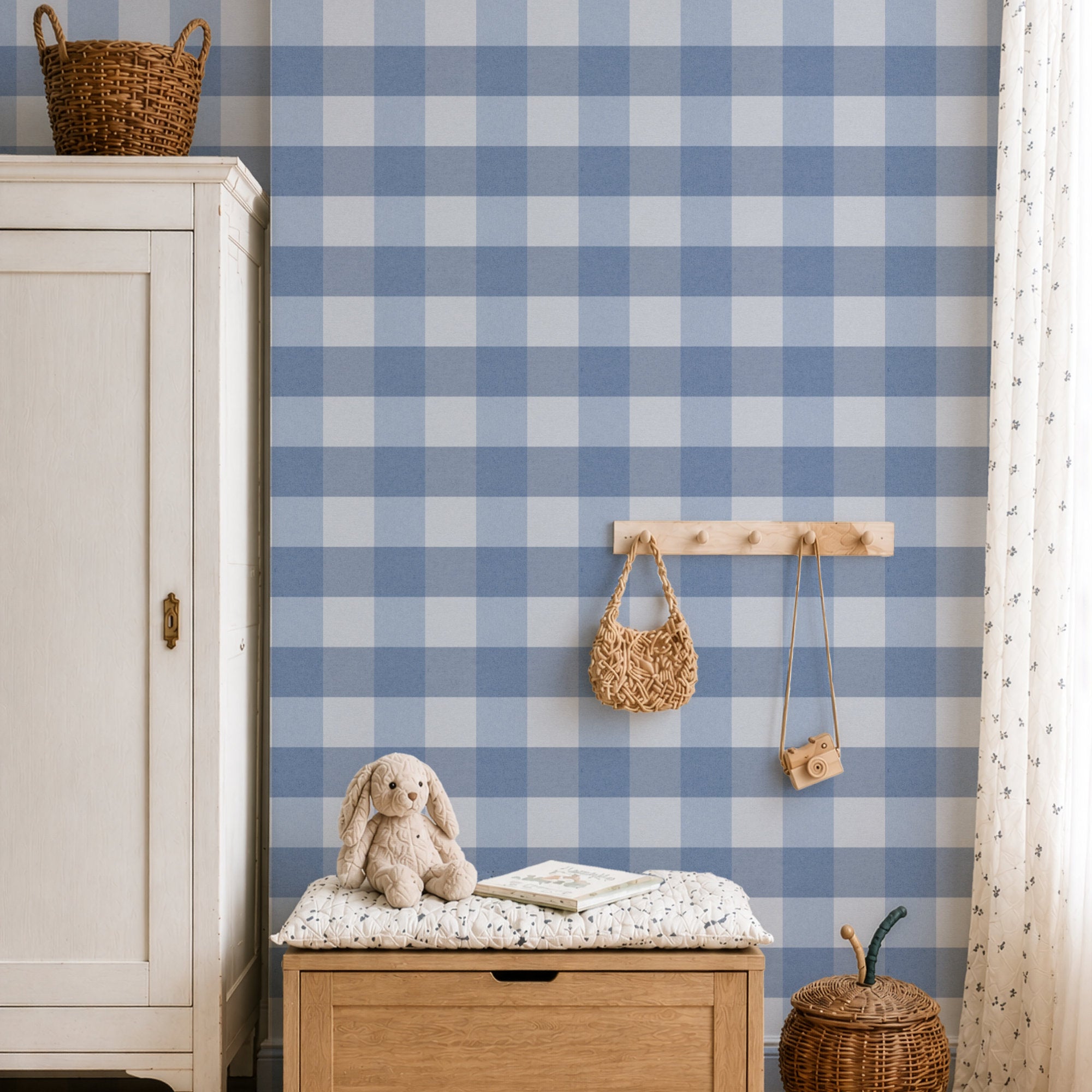 A styled children's room corner featuring a prominent blue and white checkered  gingham wallpaper. In the foreground, a light wood chest of drawers holds a white patterned cushion with a beige bunny plush toy and a book.