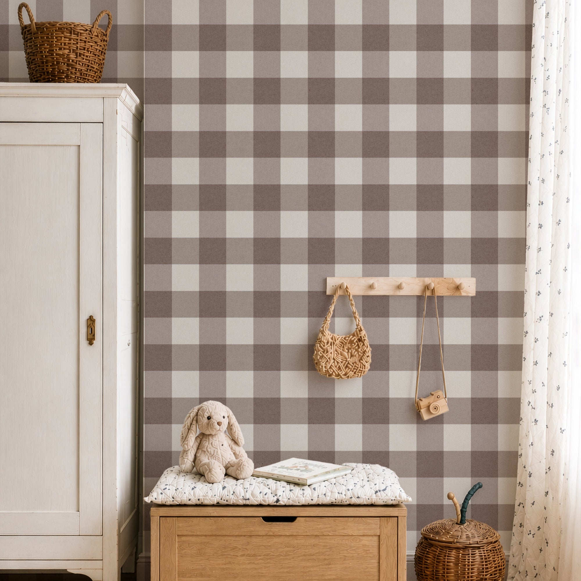 A styled children's room corner featuring brown and beige buffalo check gingham wallpaper on the wall, styled with a white wooden cabinet, a wooden bench with a bunny toy, a wooden peg rack with woven accessories, and a curtain.