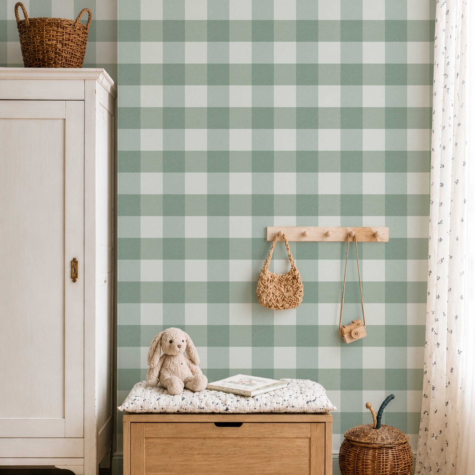 A styled nursery or playroom corner featuring sage green and white gingham wallpaper. In the foreground, a light wood storage bench with a white floral cushion holds a beige bunny plush toy and a book.