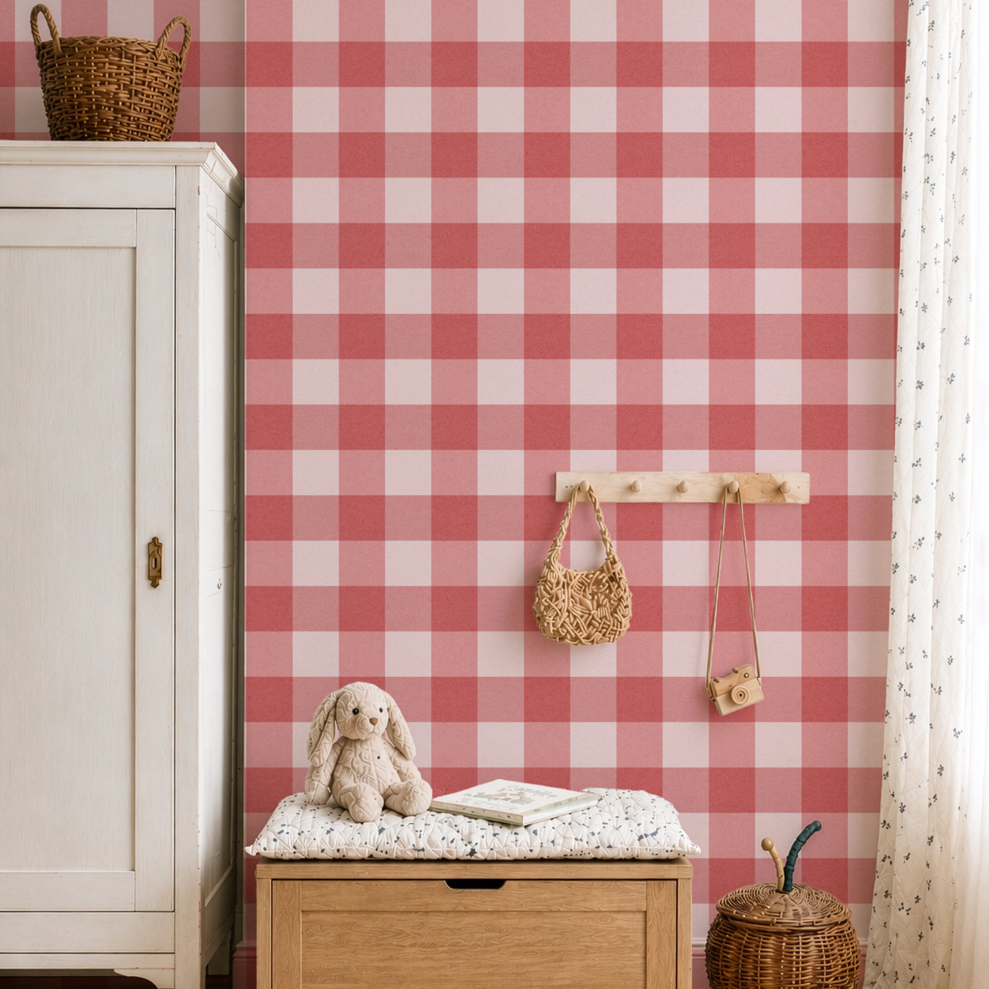 A styled interior corner featuring pink and white checkered gingham wallpaper on the wall, with a white cabinet, wooden bench, toy rabbit, woven bags, and a curtain.