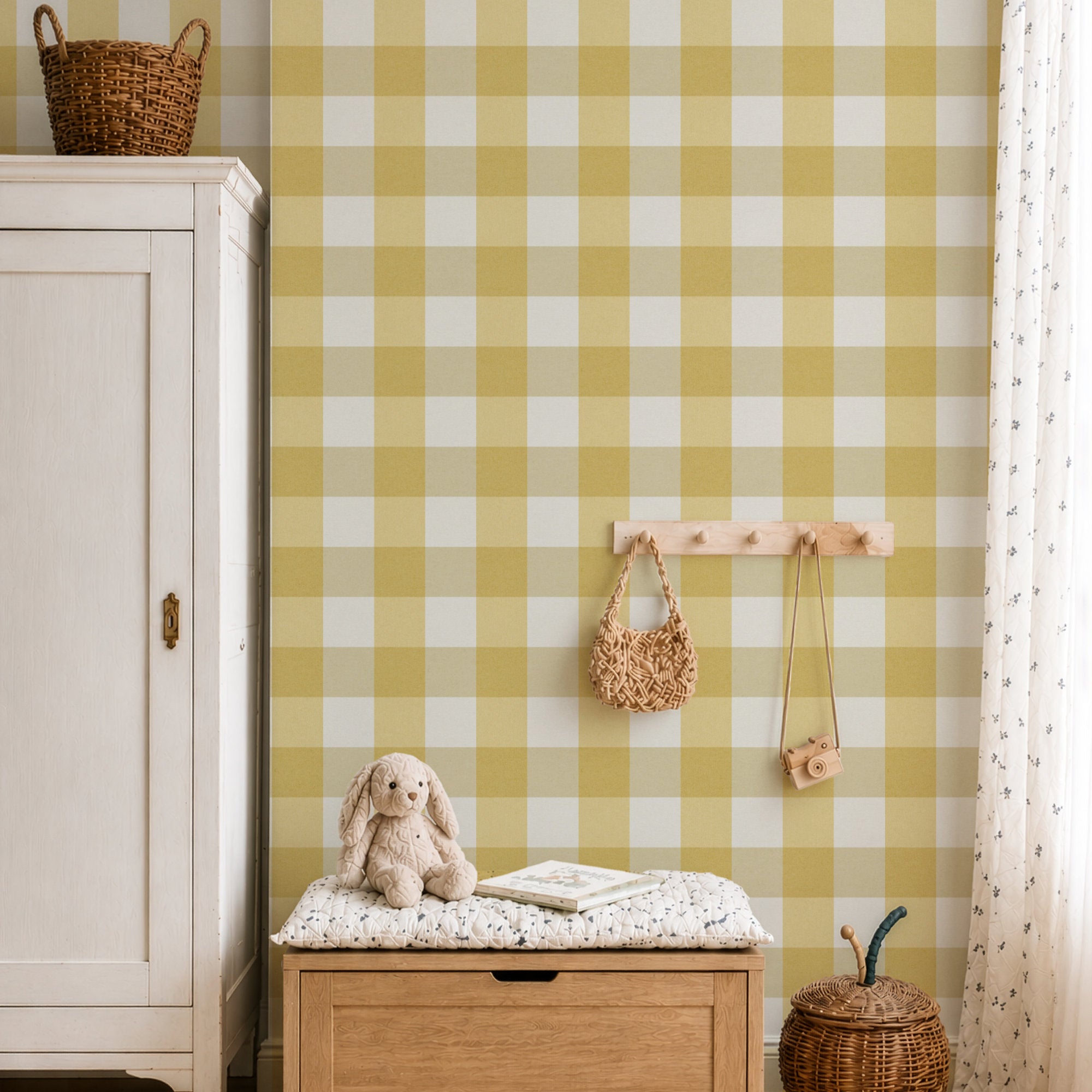 A styled nursery or playroom corner featuring a prominent mustard yellow and white gingham wallpaper. In front of the wallpaper is a light wood bench with a white patterned cushion, a stuffed bunny, and an open book.
